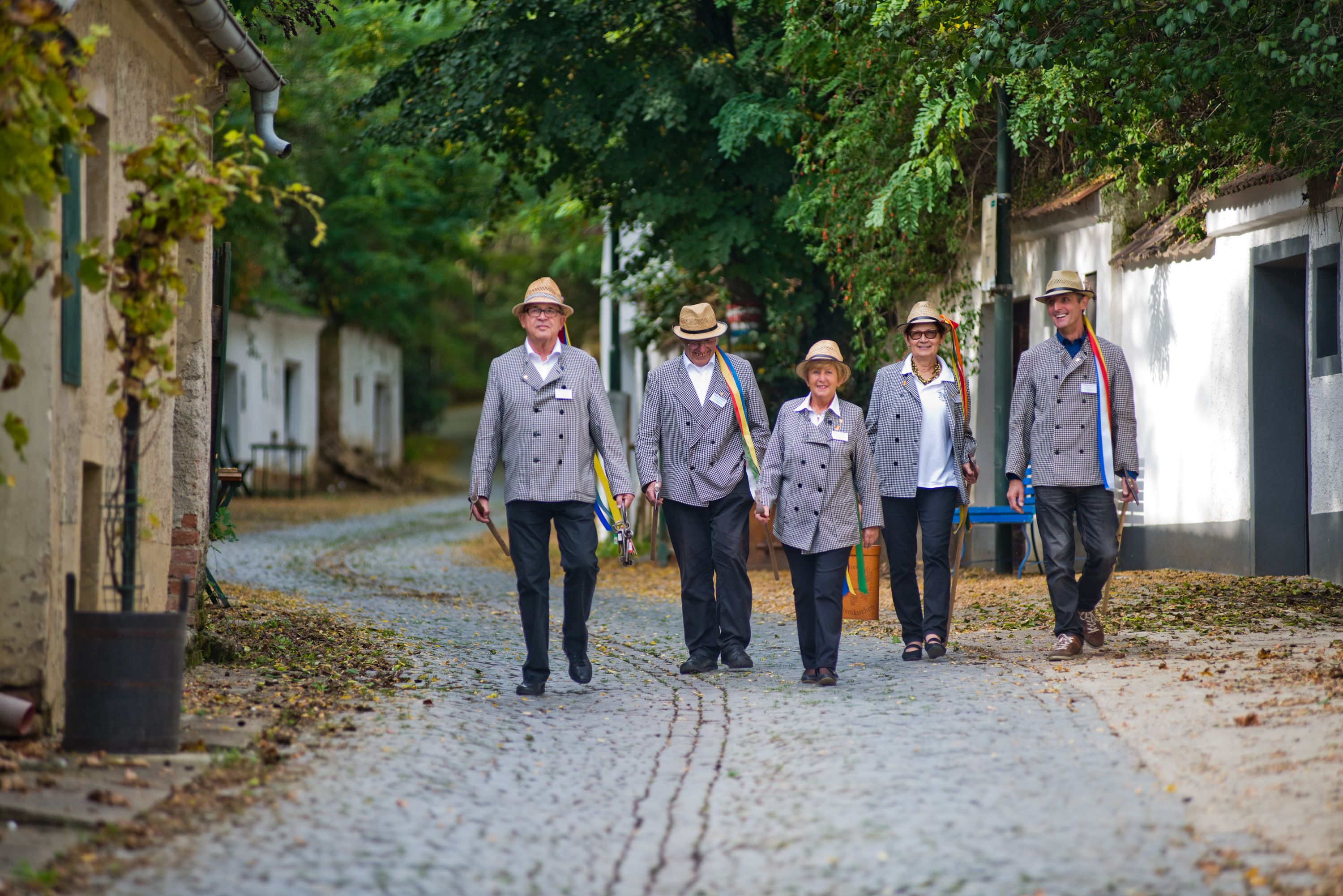 Five people in traditional dress walk along a cobbled street.