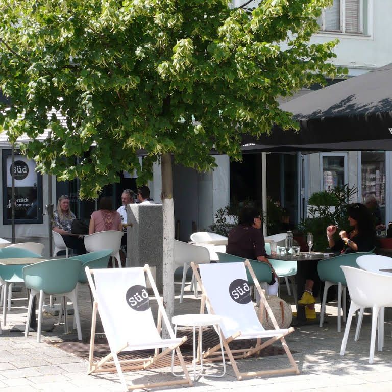 A pavement garden with chairs and deckchairs under a tree.
