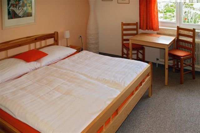 Cozy guest room with double bed, wooden furniture and a small table by the window.