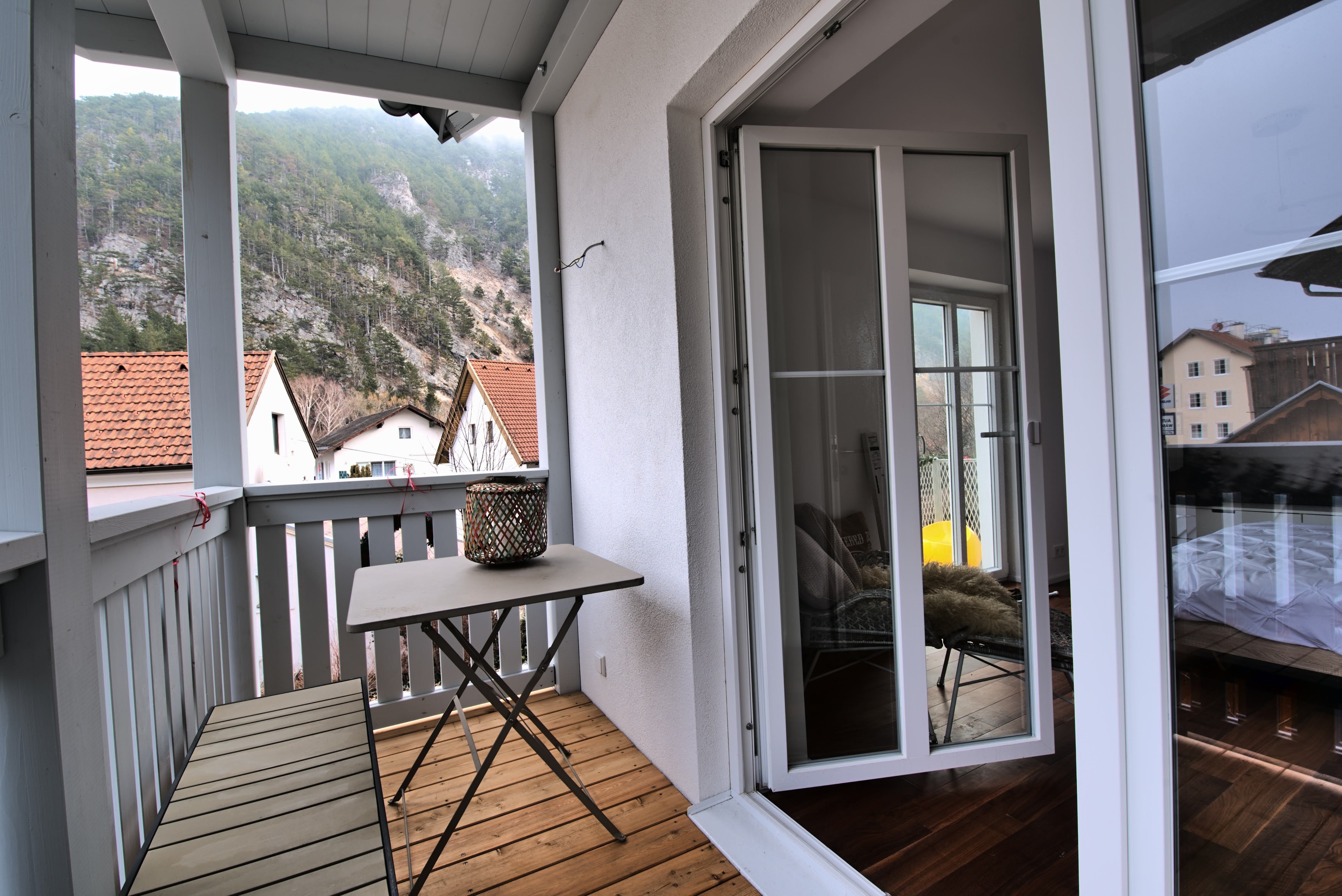 A balcony with a table and bench, surrounded by mountains and houses with red roofs.