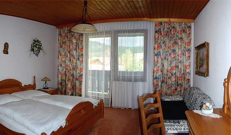 Comfortable hotel room with wooden furniture, double bed, balcony and colorful curtains.