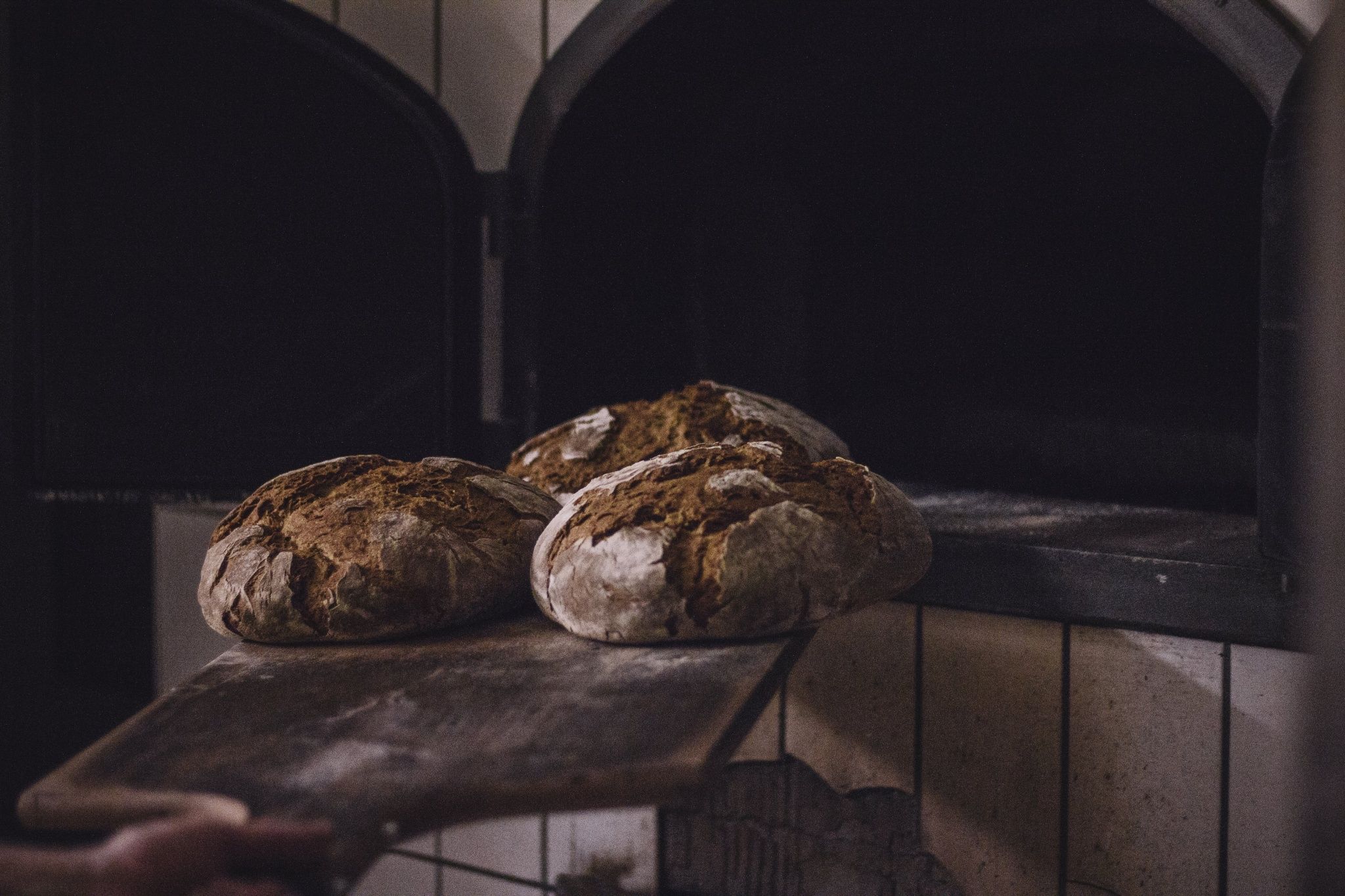 Three loaves of bread on a wooden slider in front of an oven.