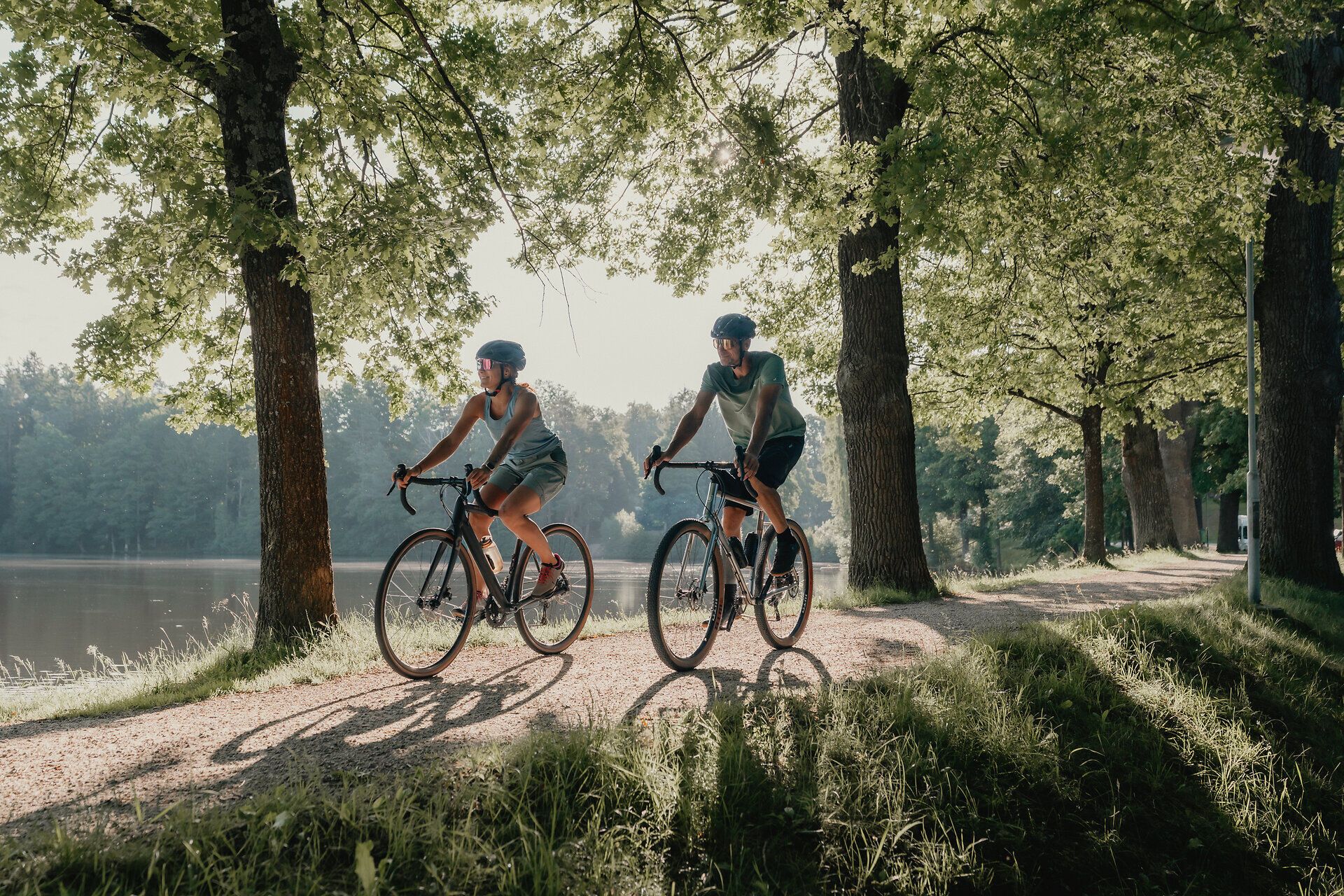 Zwei Personen, die man von vorne sieht, umgeben von Wald und Wasser, die mit ihren Rädern fahren