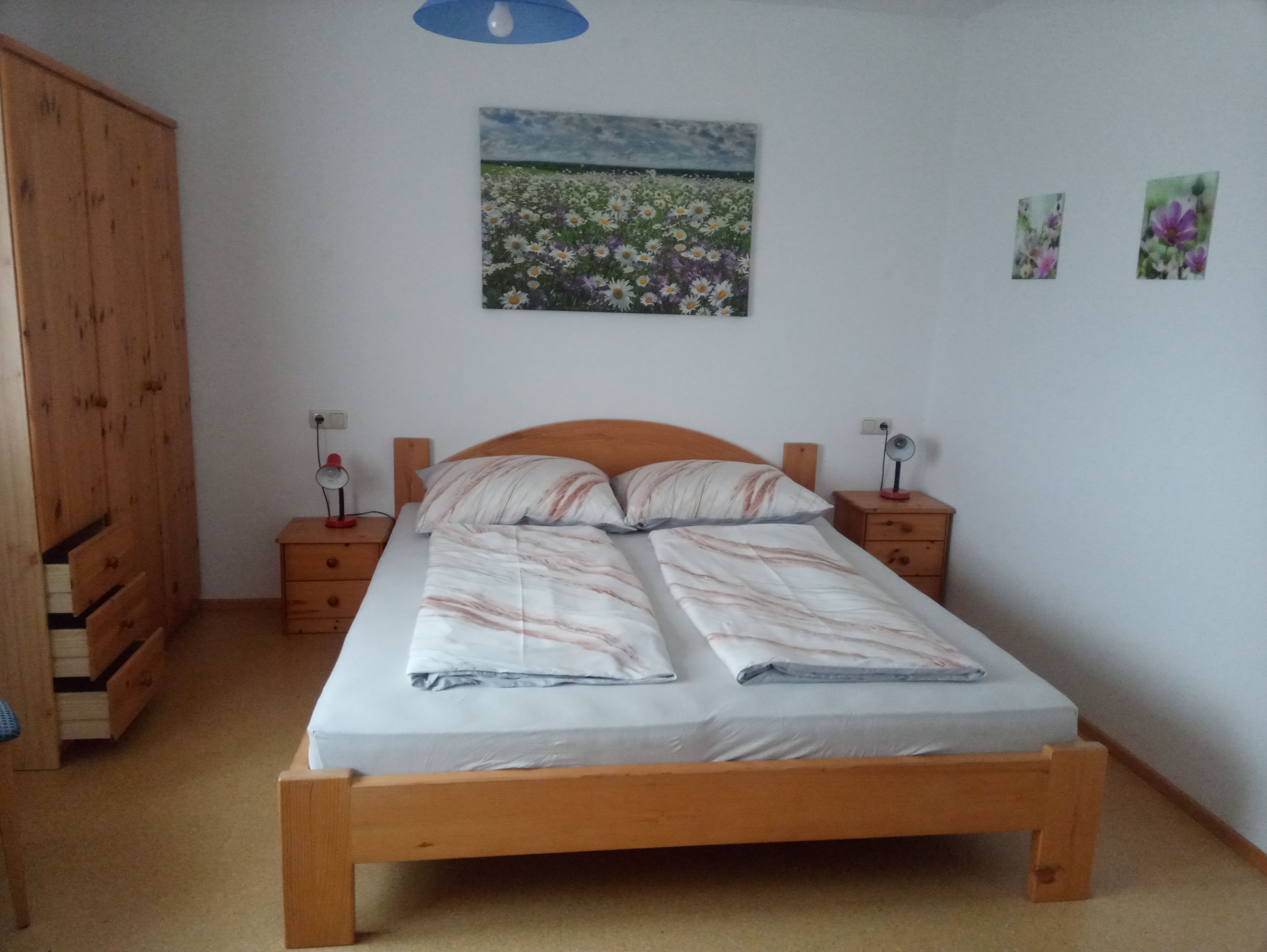 Bedroom with double bed, wooden furniture and flower pictures on the wall.