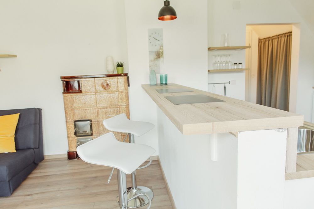 Modern kitchen with bar counter and two white bar stools, next to a traditional oven.