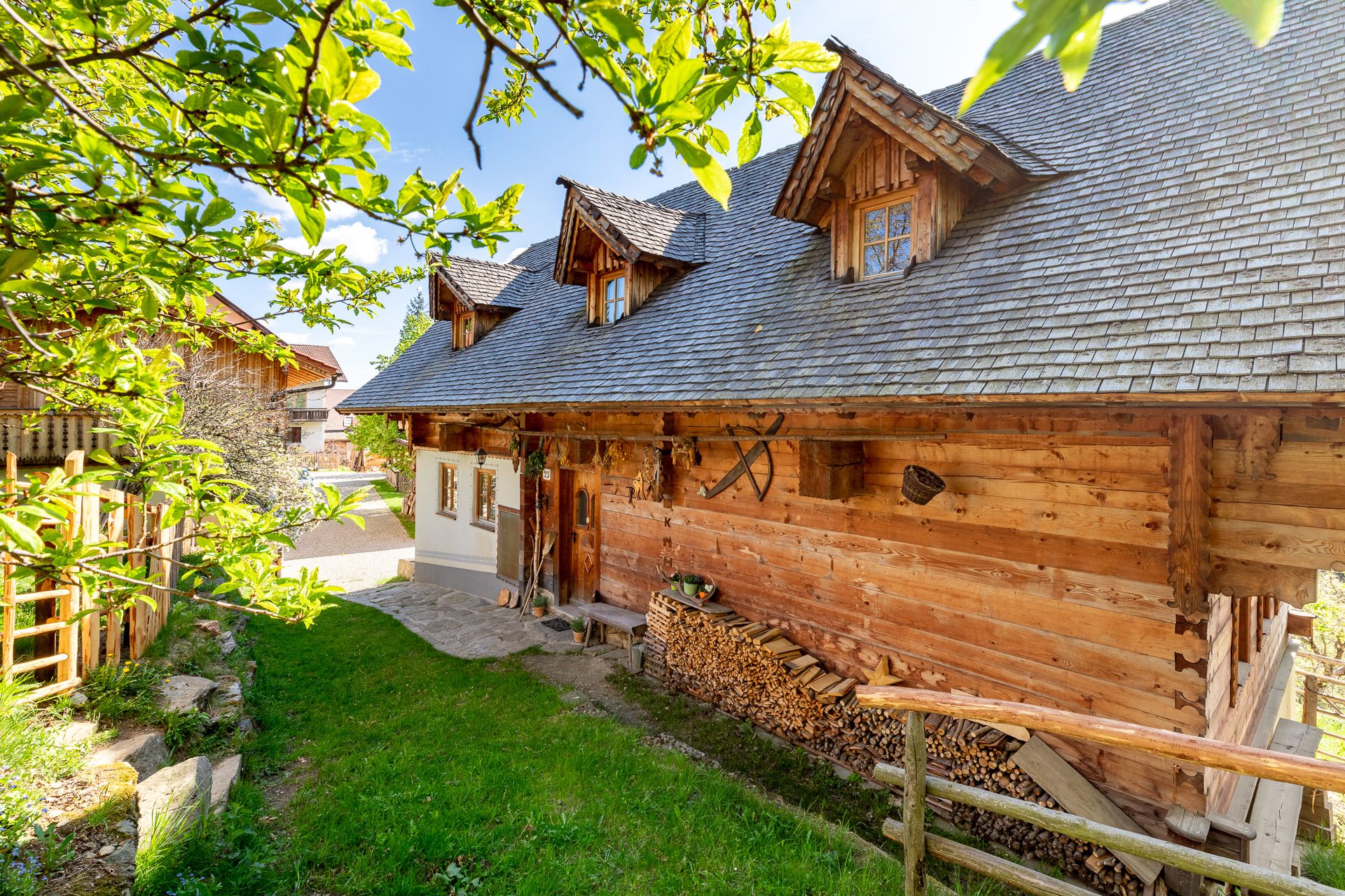 Traditional wooden house with woodpile and wooden fence surrounded by green nature.