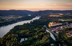 Die sanften Hügel und die glitzernde Donau umarmen das majestätische Stift Melk, während die goldenen Strahlen der Abendsonne die Landschaft in ein warmes Licht tauchen. Hier, wo Geschichte und Natur harmonisch verschmelzen, lädt die Umgebung zu unvergesslichen Erlebnissen ein.