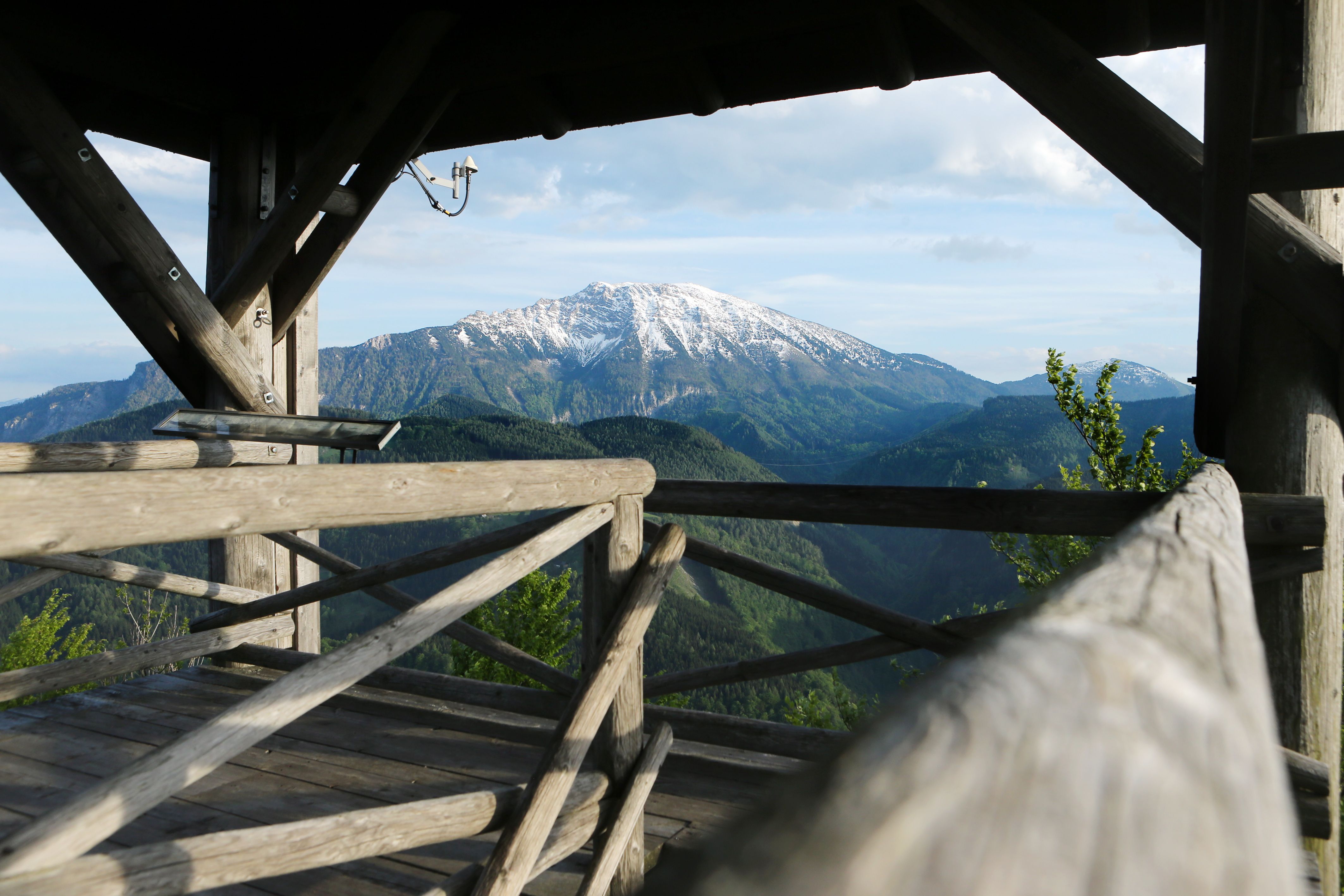 Wooden platform with a view of the snow-covered mountain and wooded hills.