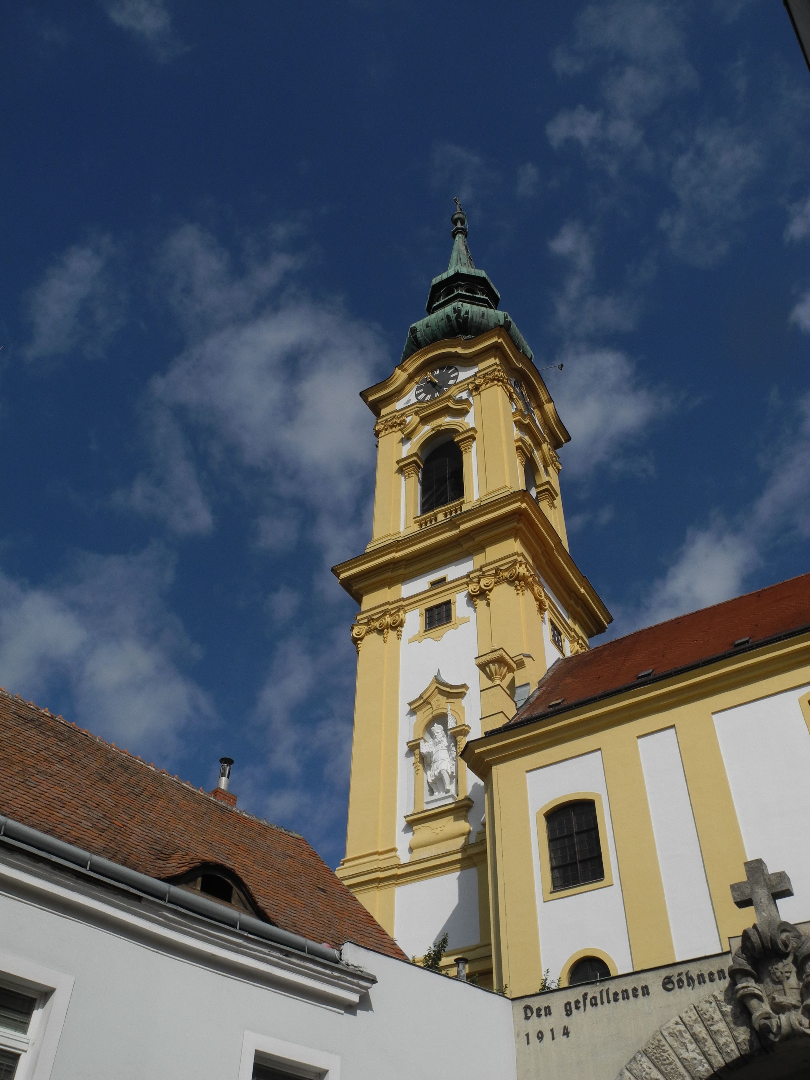 Yellow steeple of the Stockerau parish church against a blue sky.