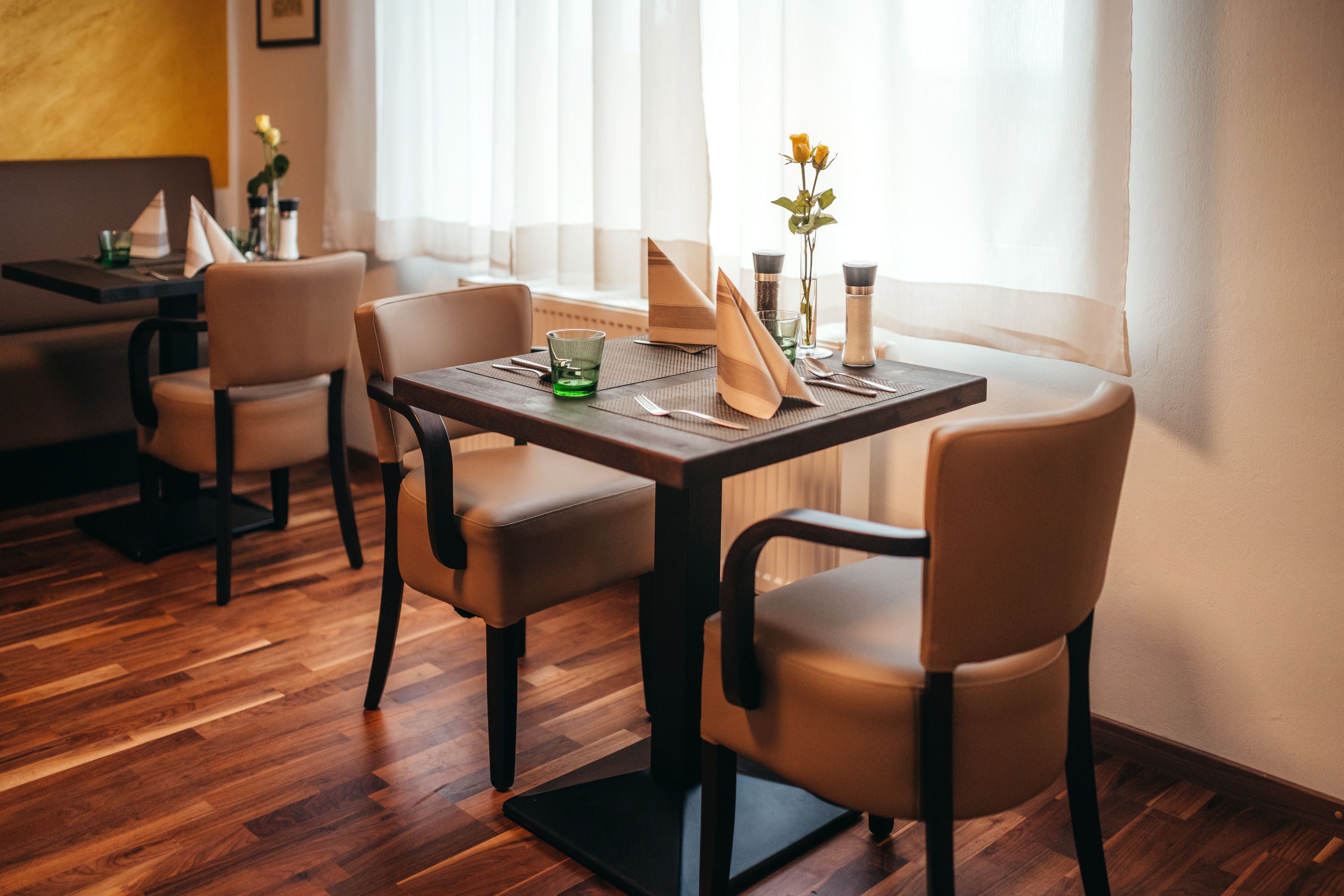 Cozy restaurant with wooden floor, laid table and flowers.
