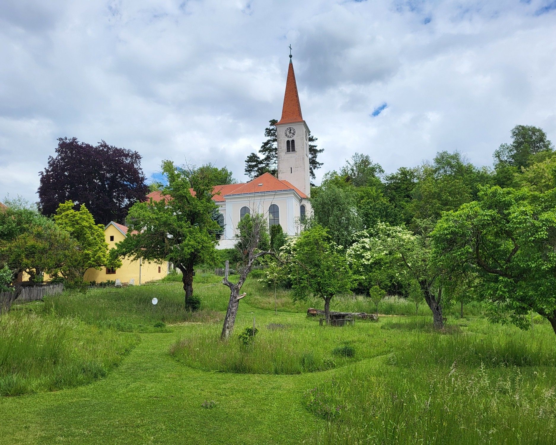 Parish garden in Königsbrunn am Wagram with a view of the historic church, surrounded by green meadows, old fruit trees and a natural garden landscape.