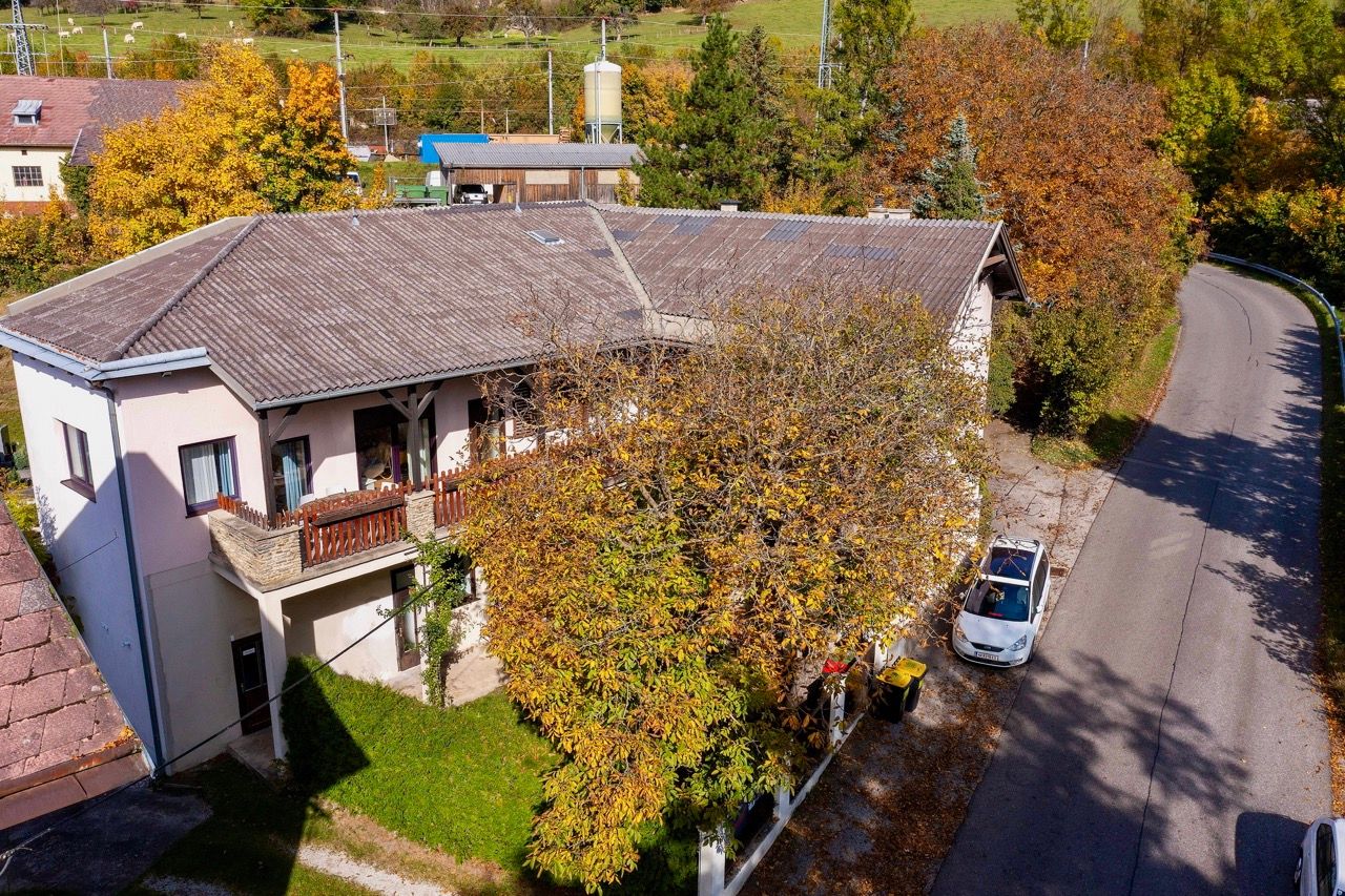 Aerial view of a two-story building with a balcony, surrounded by autumnal trees and a street.