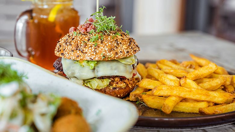 A plate of burgers and fries, a drink with lemon in the background.