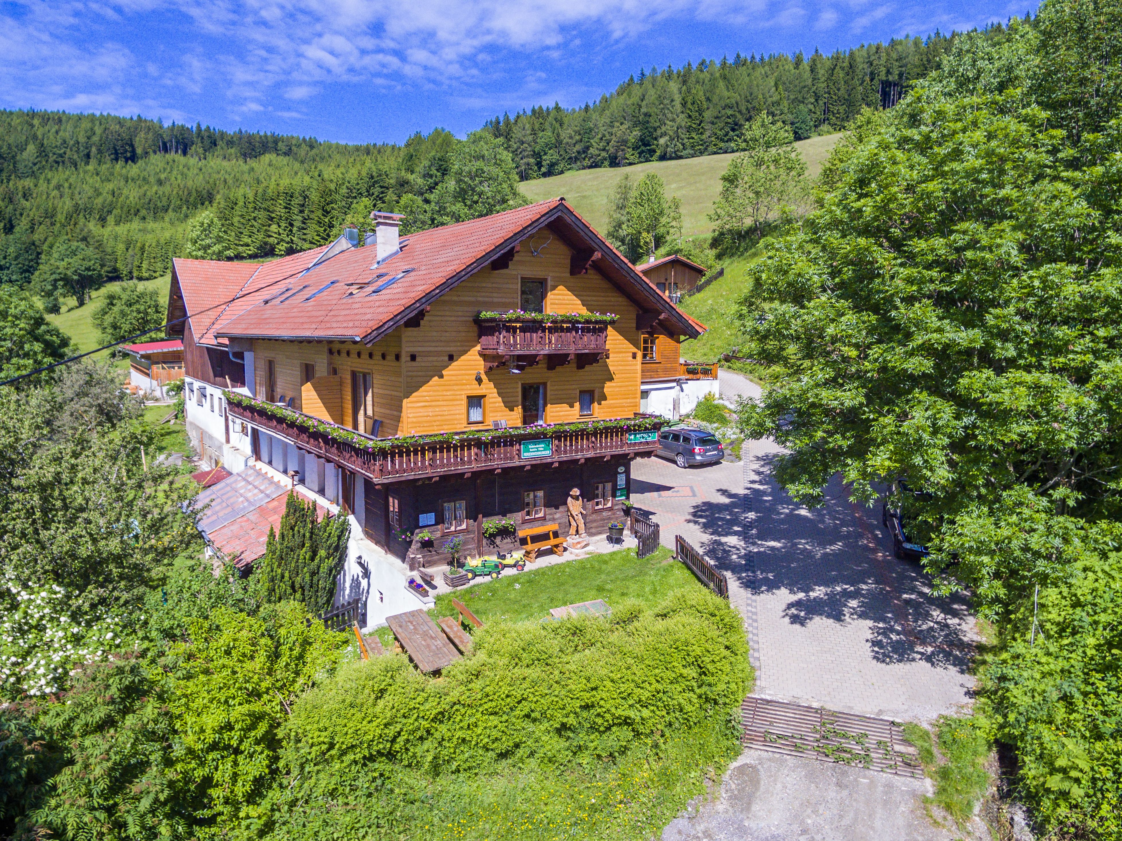 A traditional wooden house in a green, hilly landscape with trees and a blue sky.