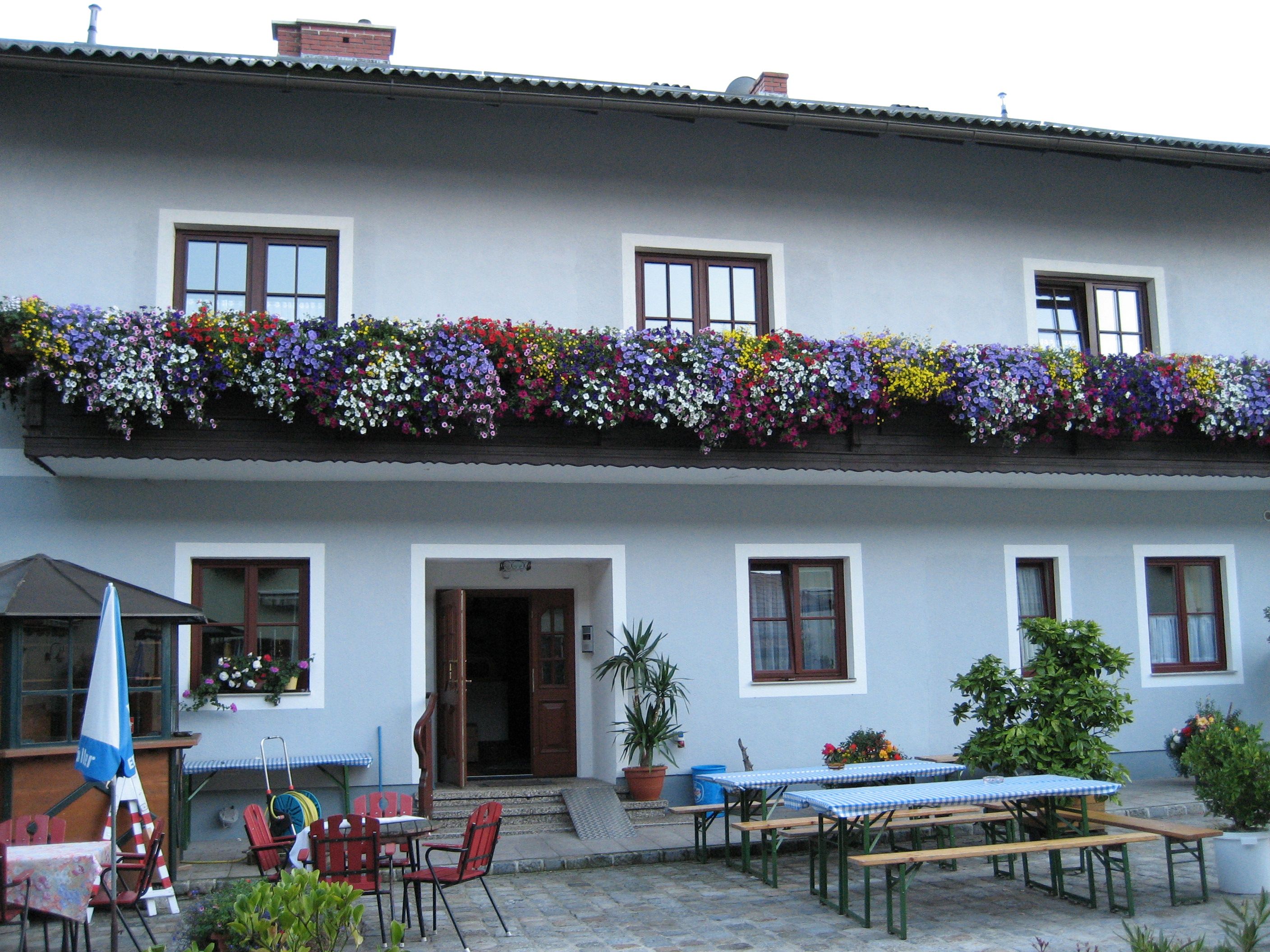 Inn with blue façade, flower boxes on the balcony and beer garden furniture in the foreground.