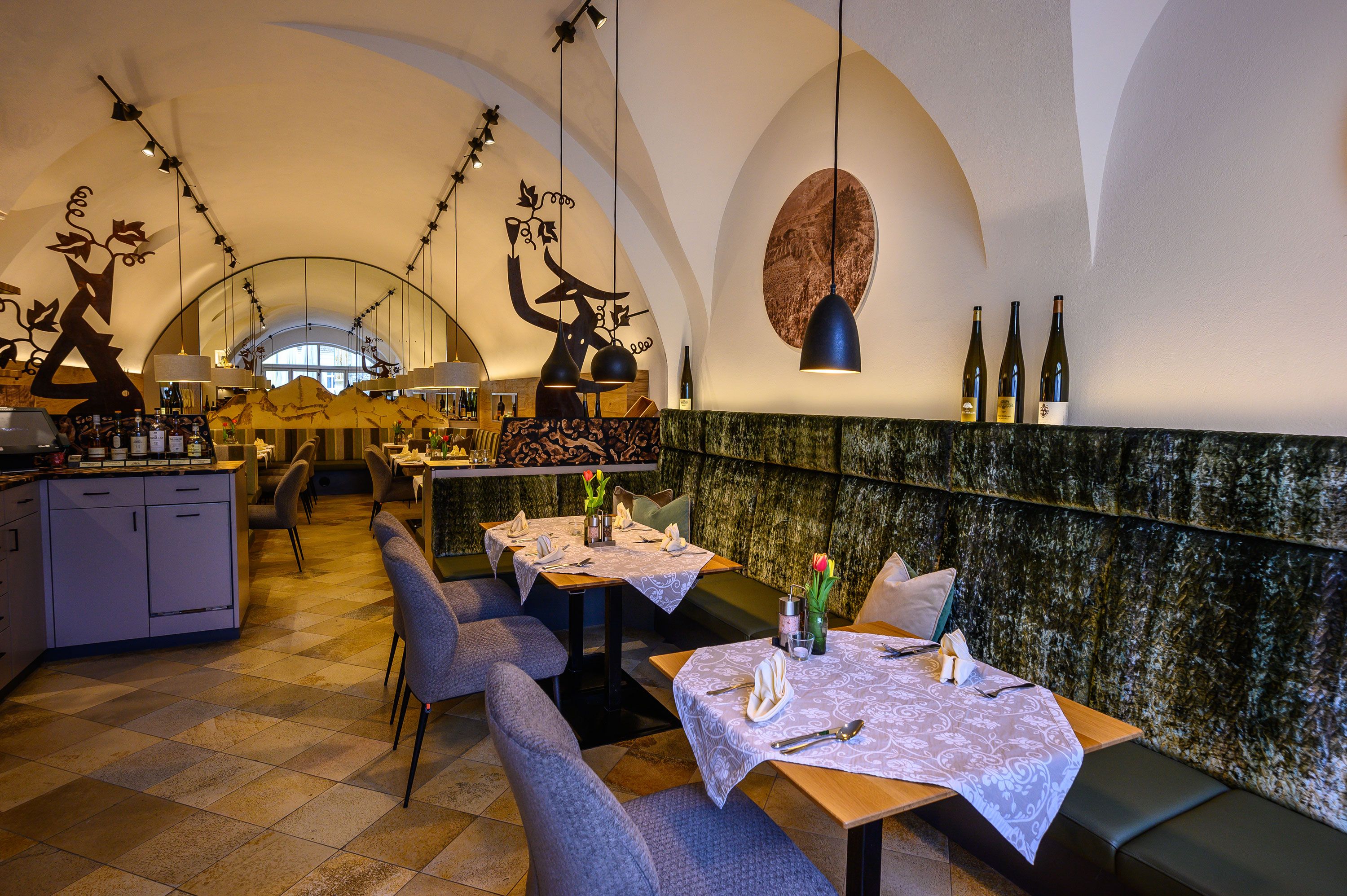 Elegant restaurant with laid tables, decorative elements and wine bottles on a shelf.