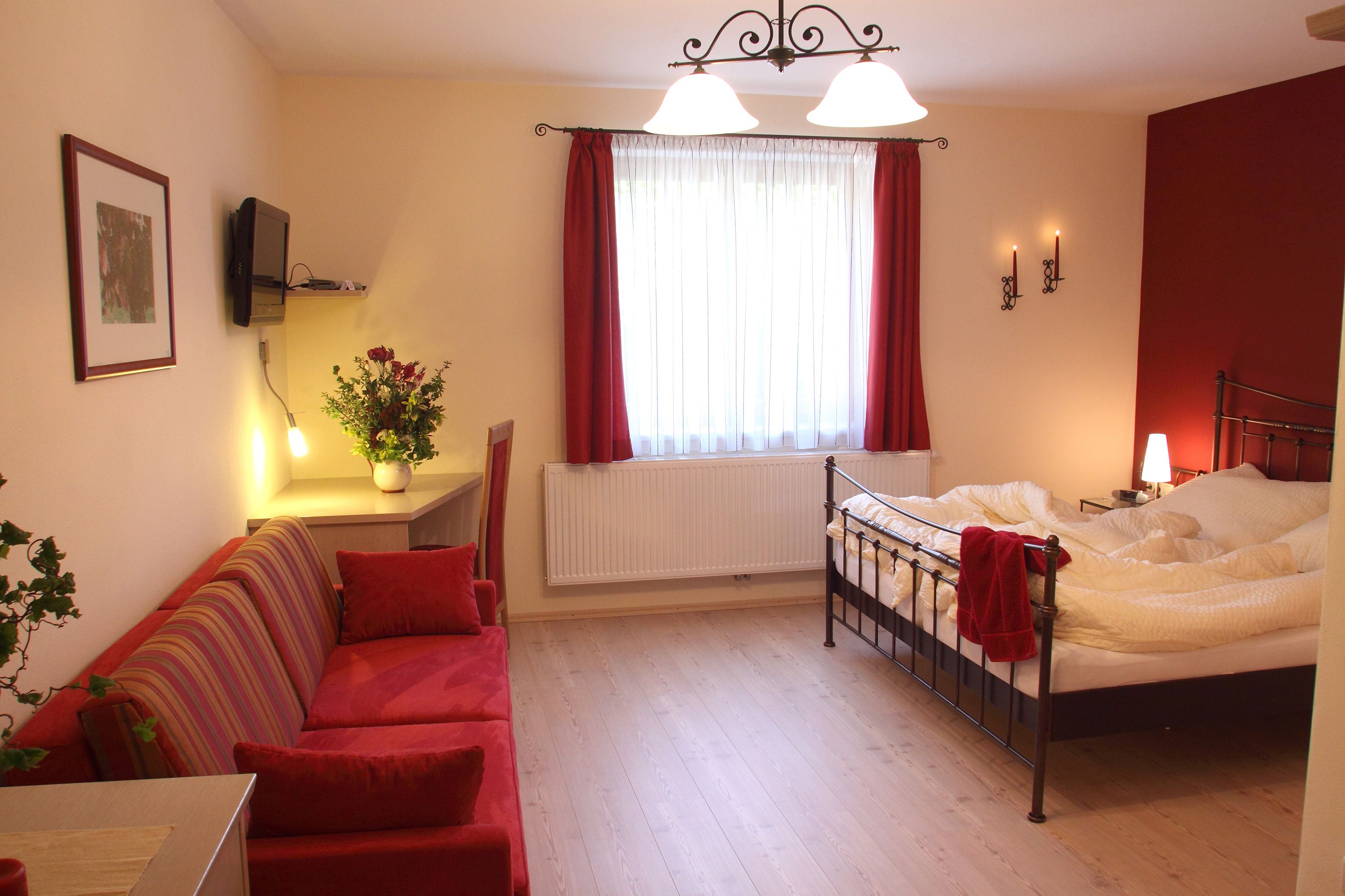 Comfortable hotel room with double bed, red sofa and desk.
