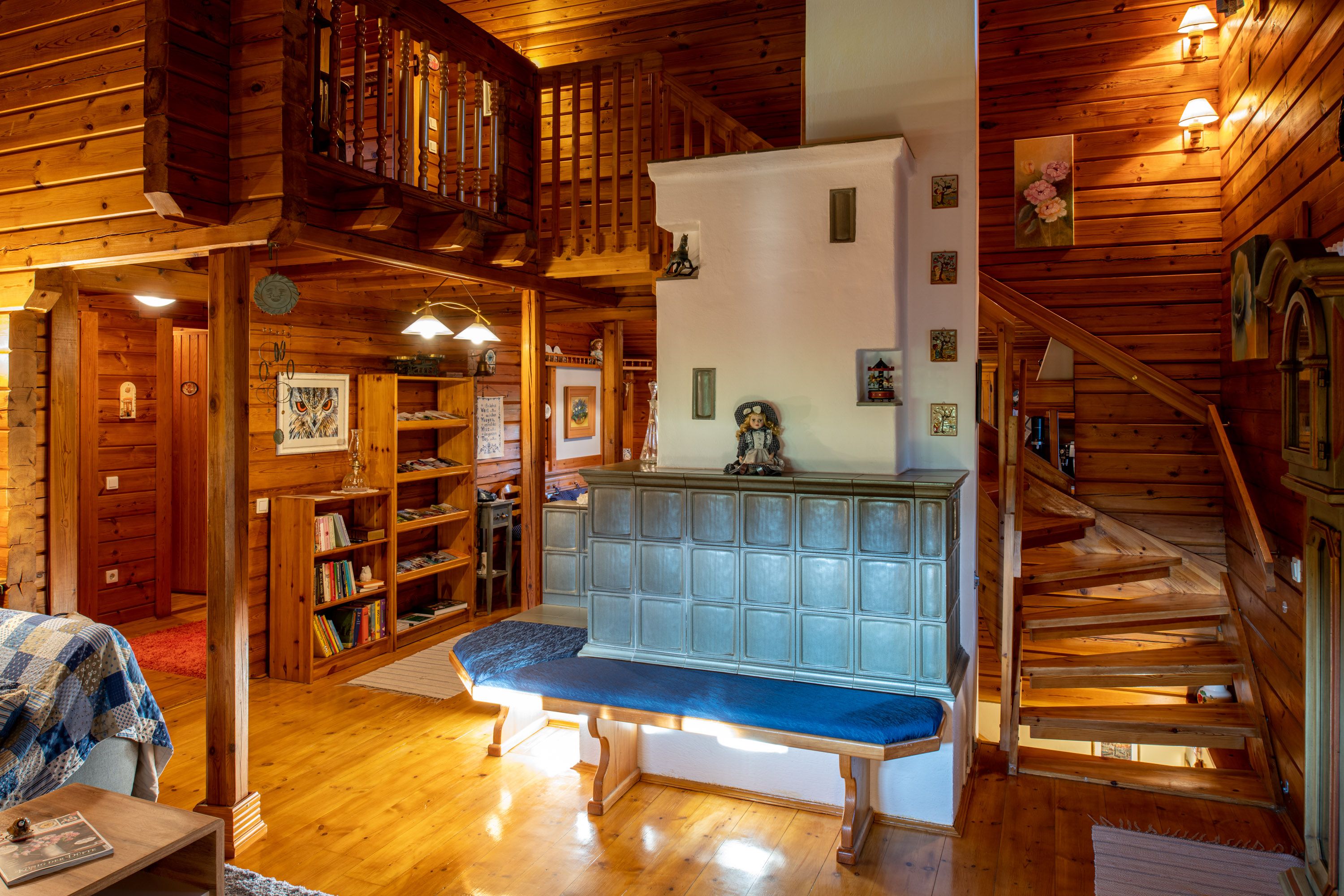 Cozy living room with tiled stove, wooden walls and staircase.