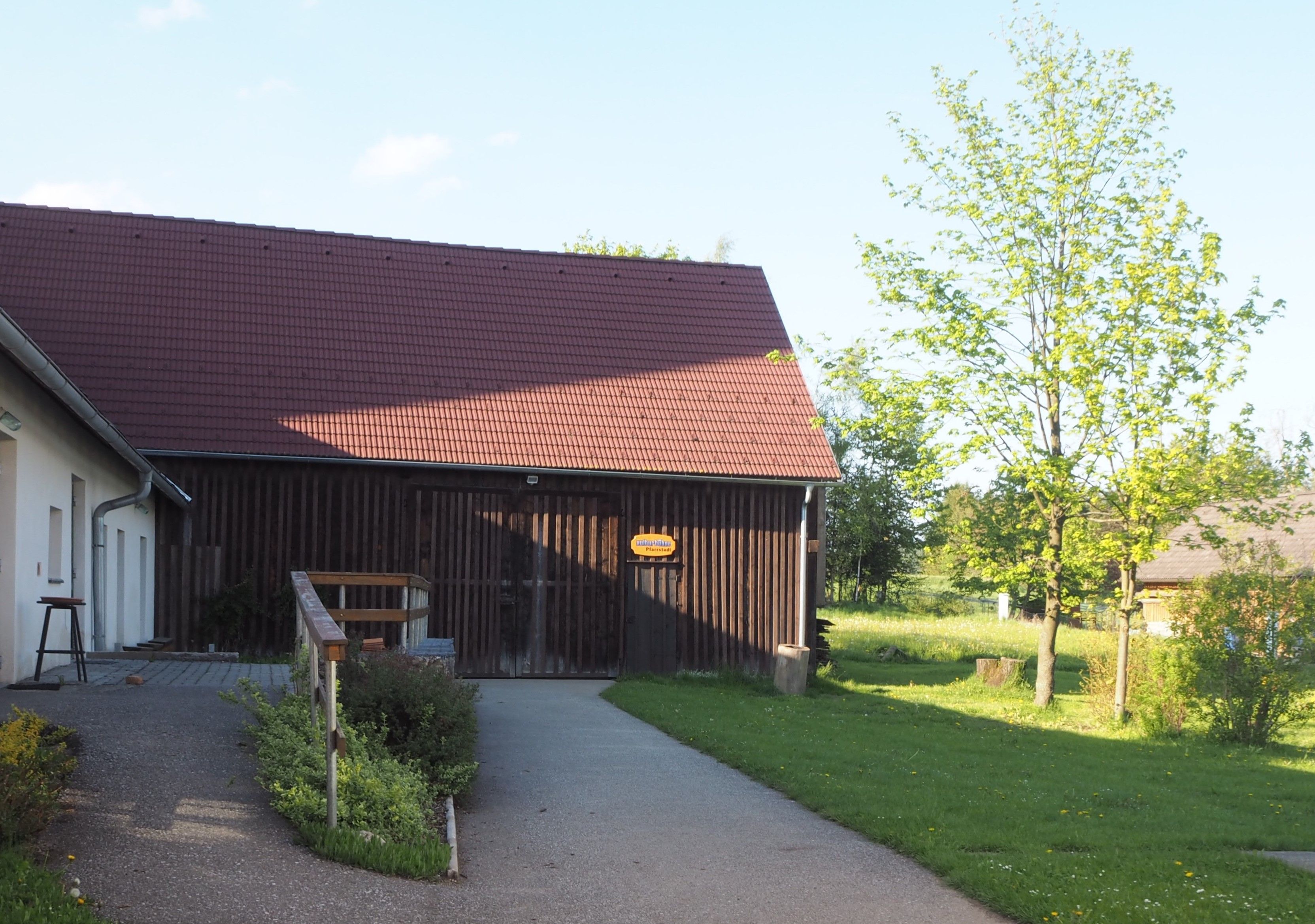 A building with a red roof and wooden walls, surrounded by green landscape and trees.
