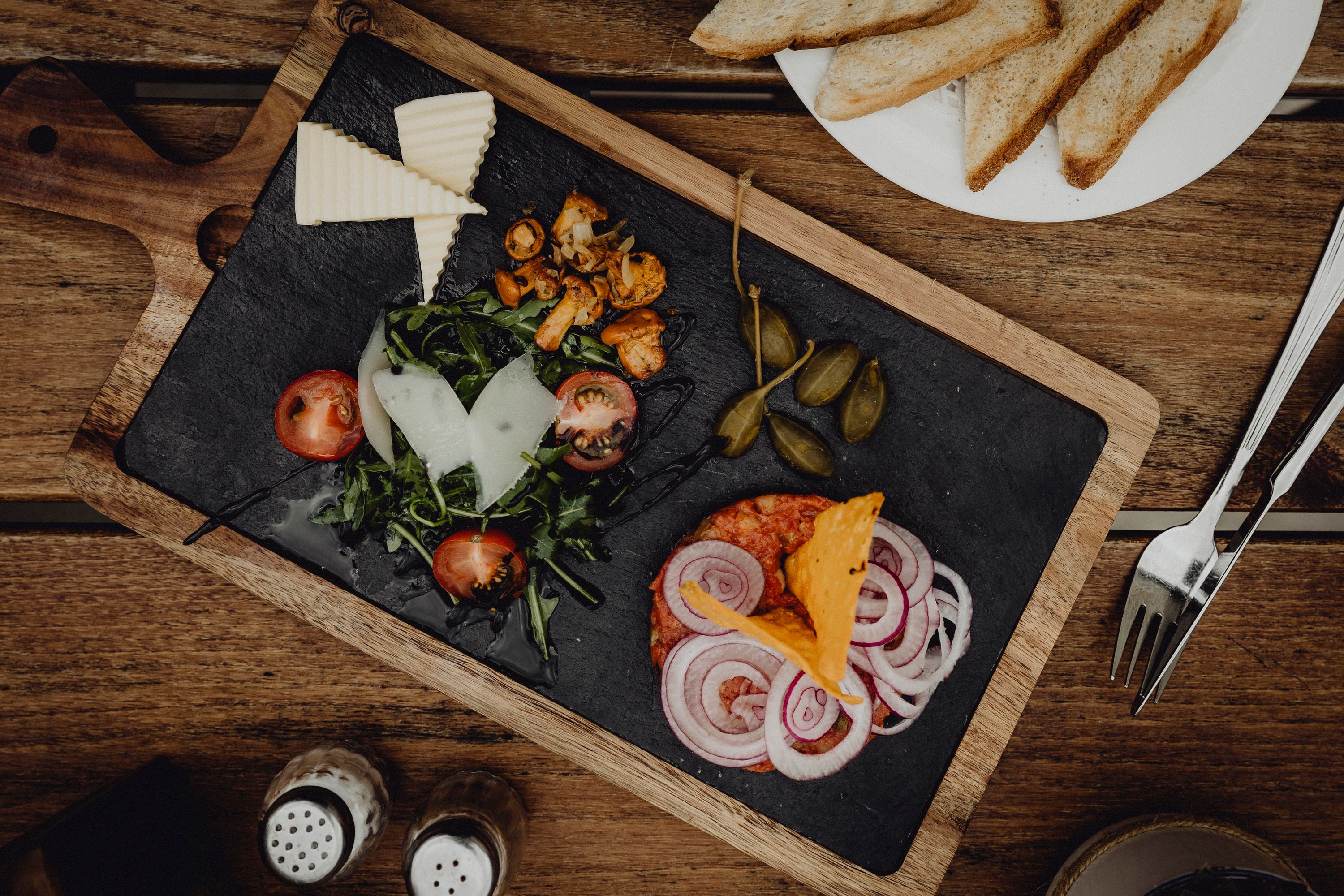 Appetizer platter with cheese, lettuce, tomatoes, onions and capers on a wooden board.