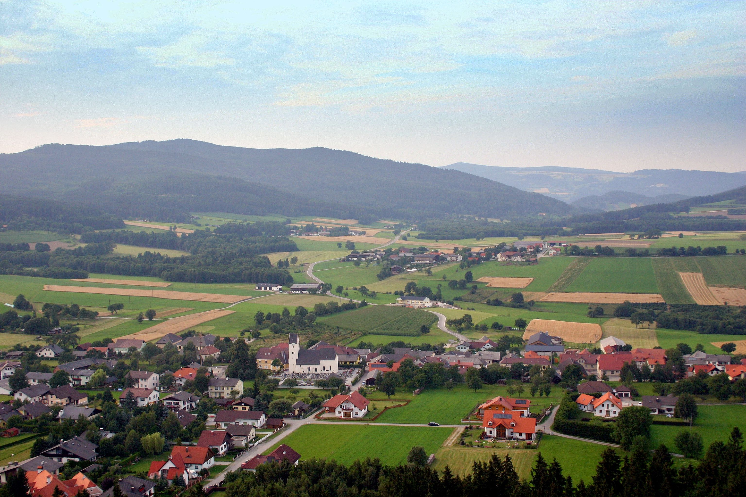 Landscape view of Münichreith am Ostrong with fields, houses and hills in the background.