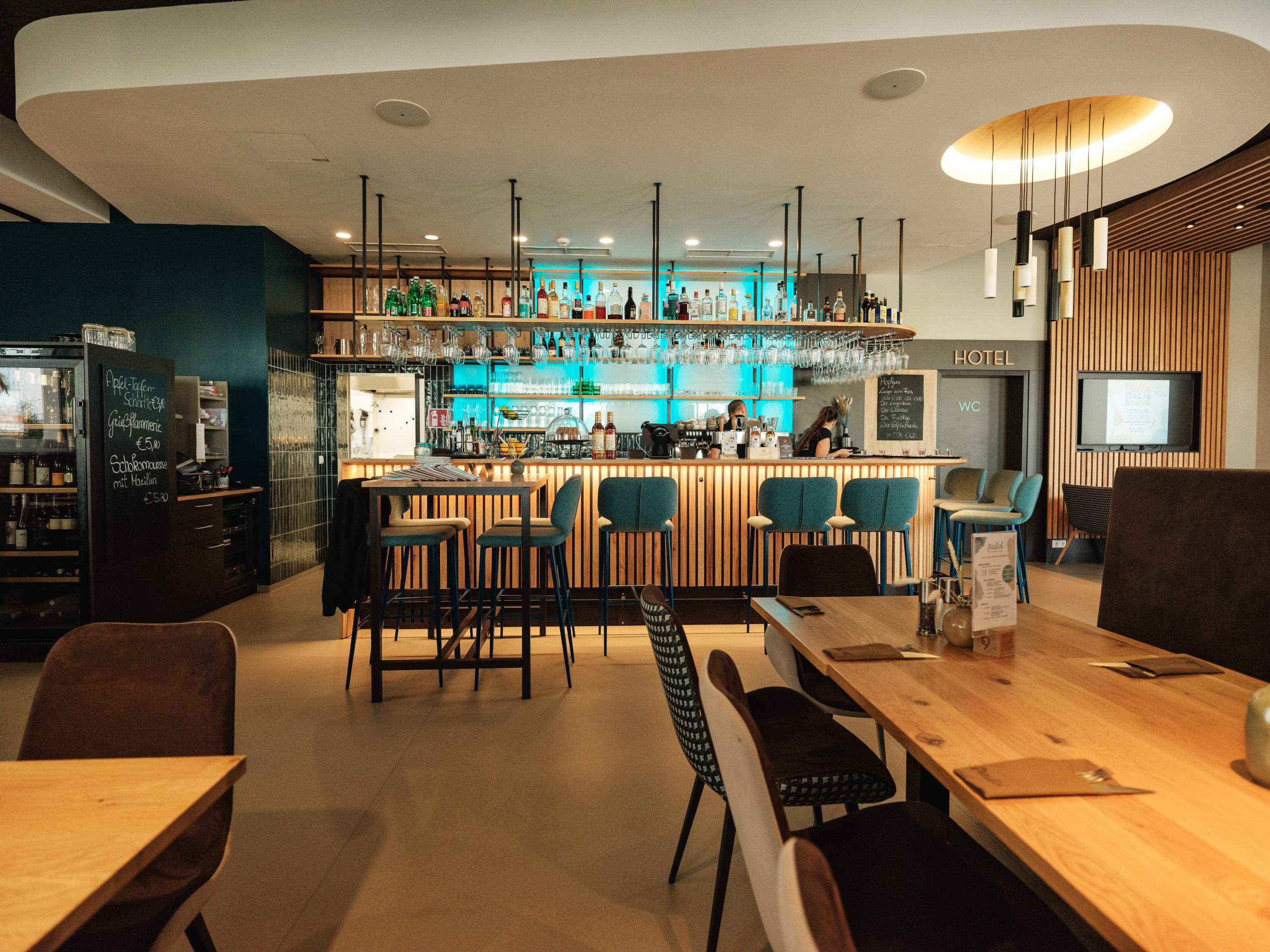 Modern bar area with wooden tables and blue bar stools, illuminated by hanging lamps.