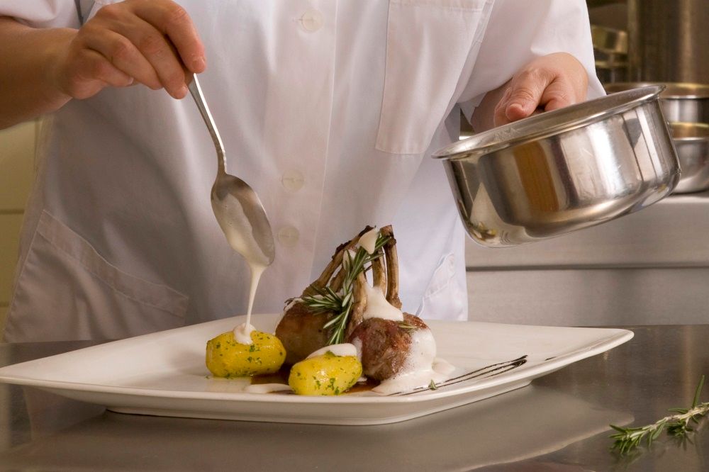 A chef prepares a dish of lamb chops and potatoes on a plate.