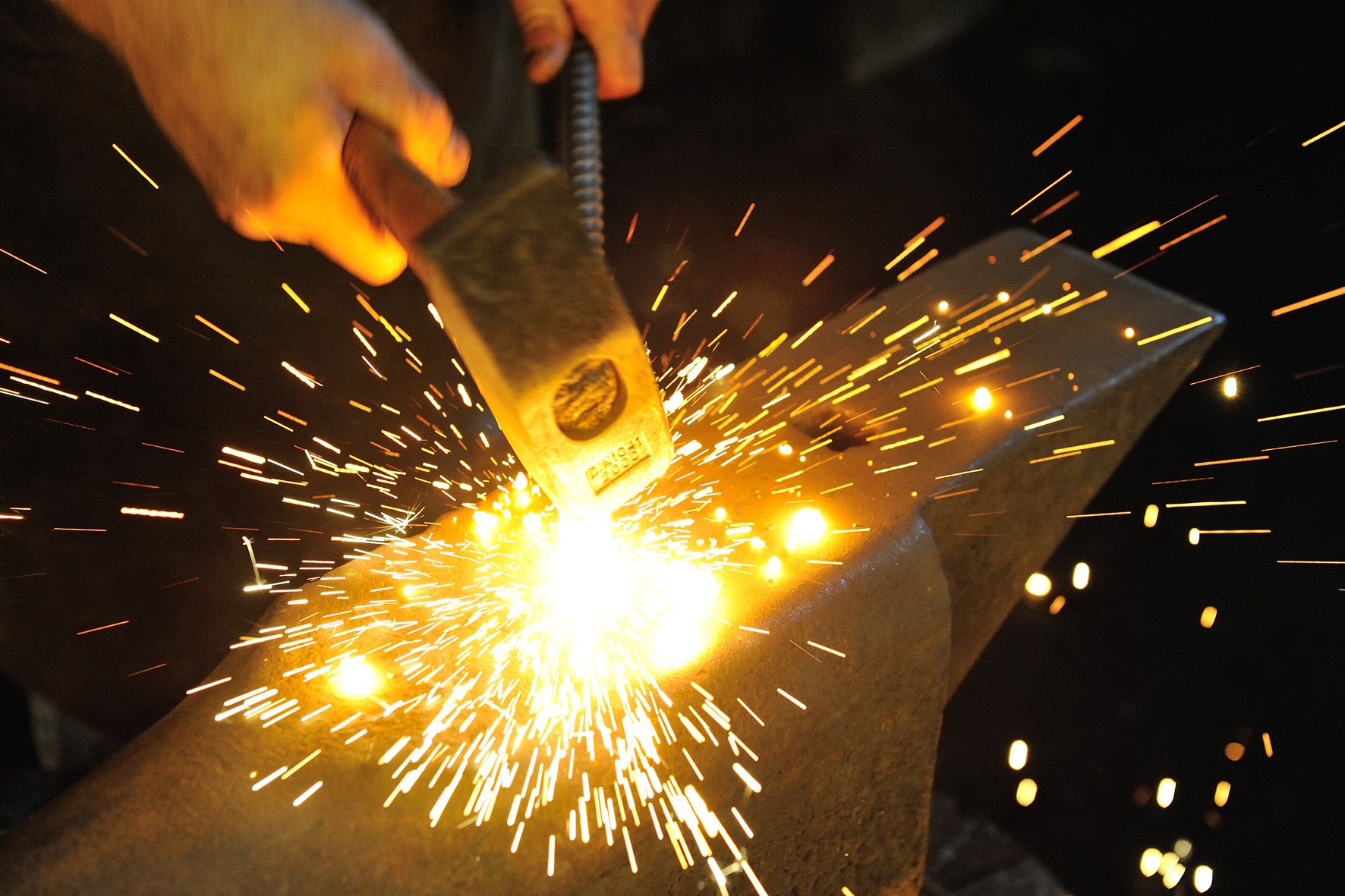A blacksmith strikes red-hot metal on an anvil with a hammer, sparks fly.