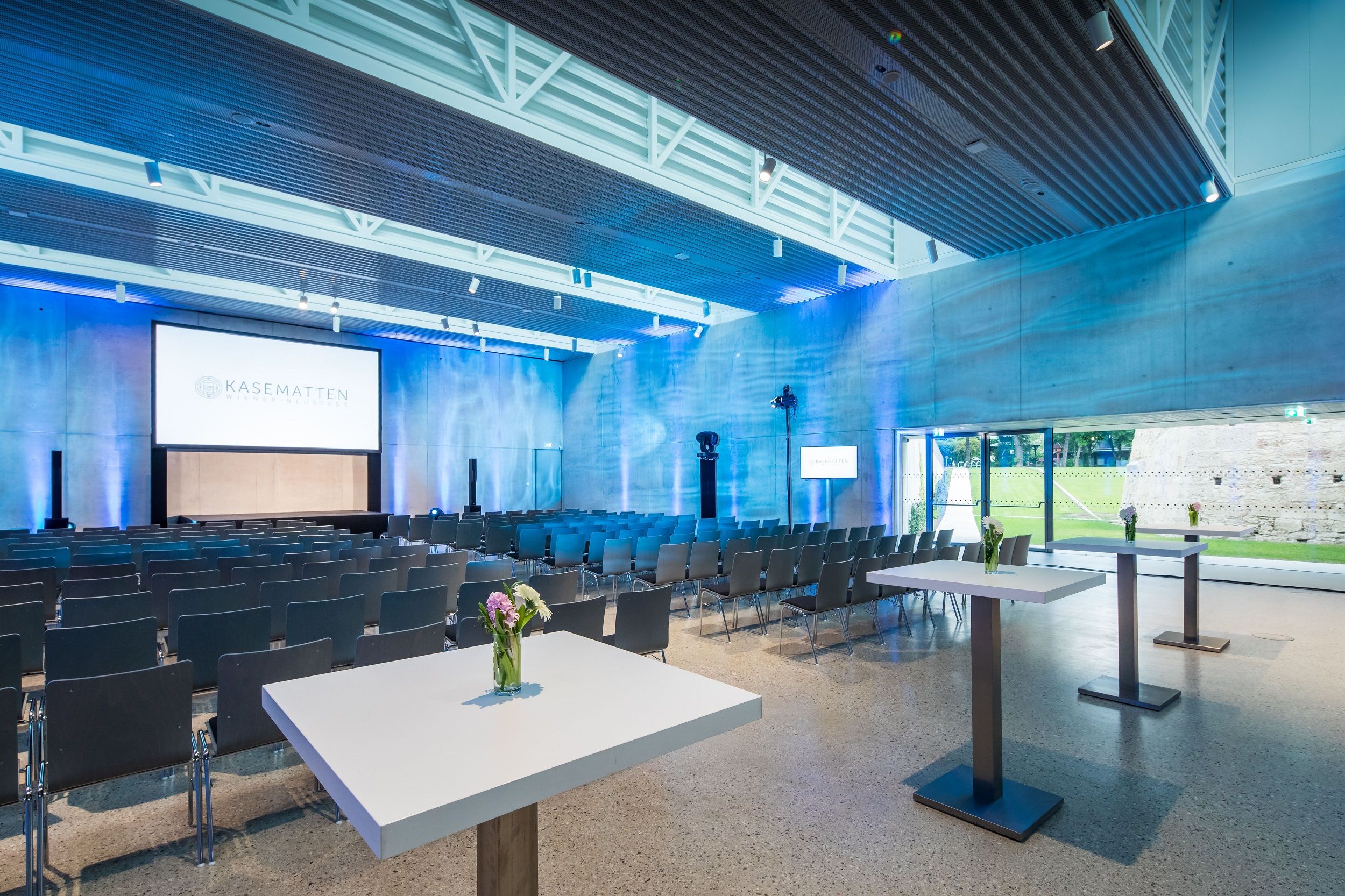 Modern conference room with chairs, tables and screen, illuminated in blue.