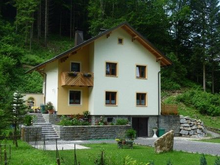 A yellow guest house with a wooden balcony, surrounded by green nature and trees.