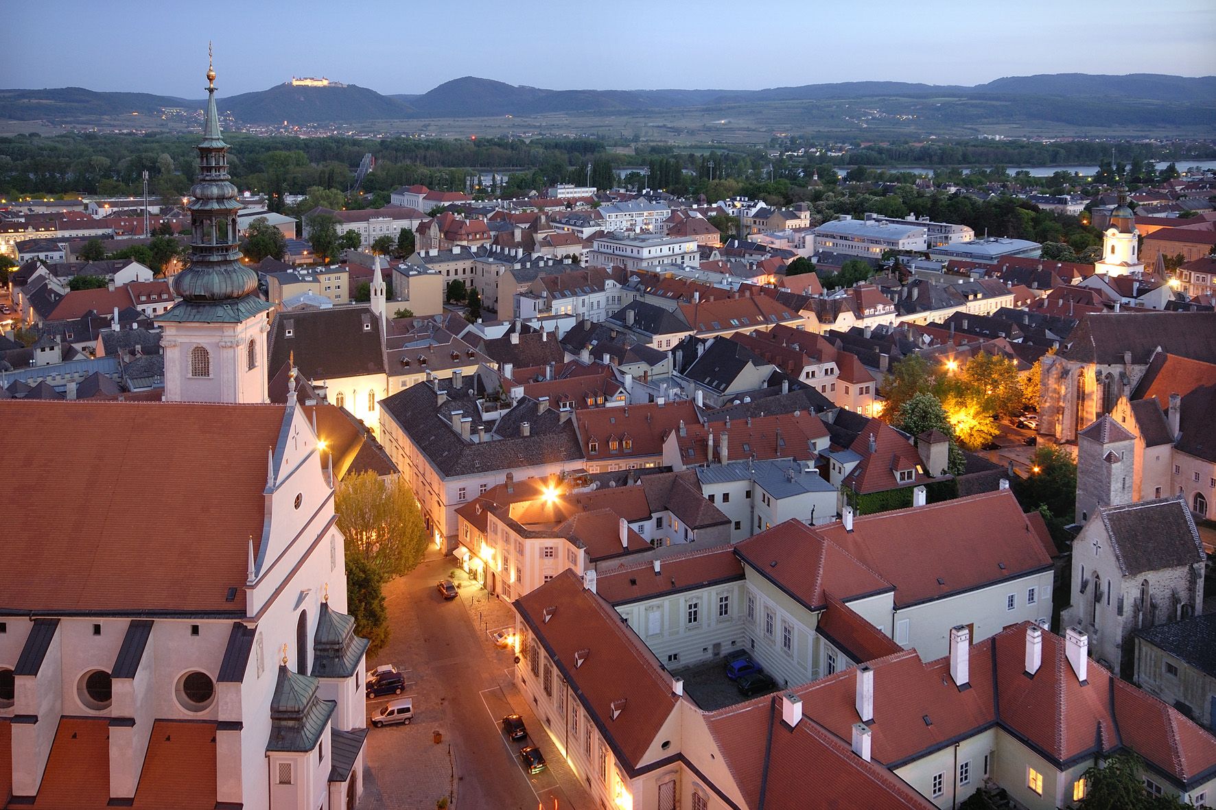 Evening city view of Krems with illuminated buildings and hills in the background.