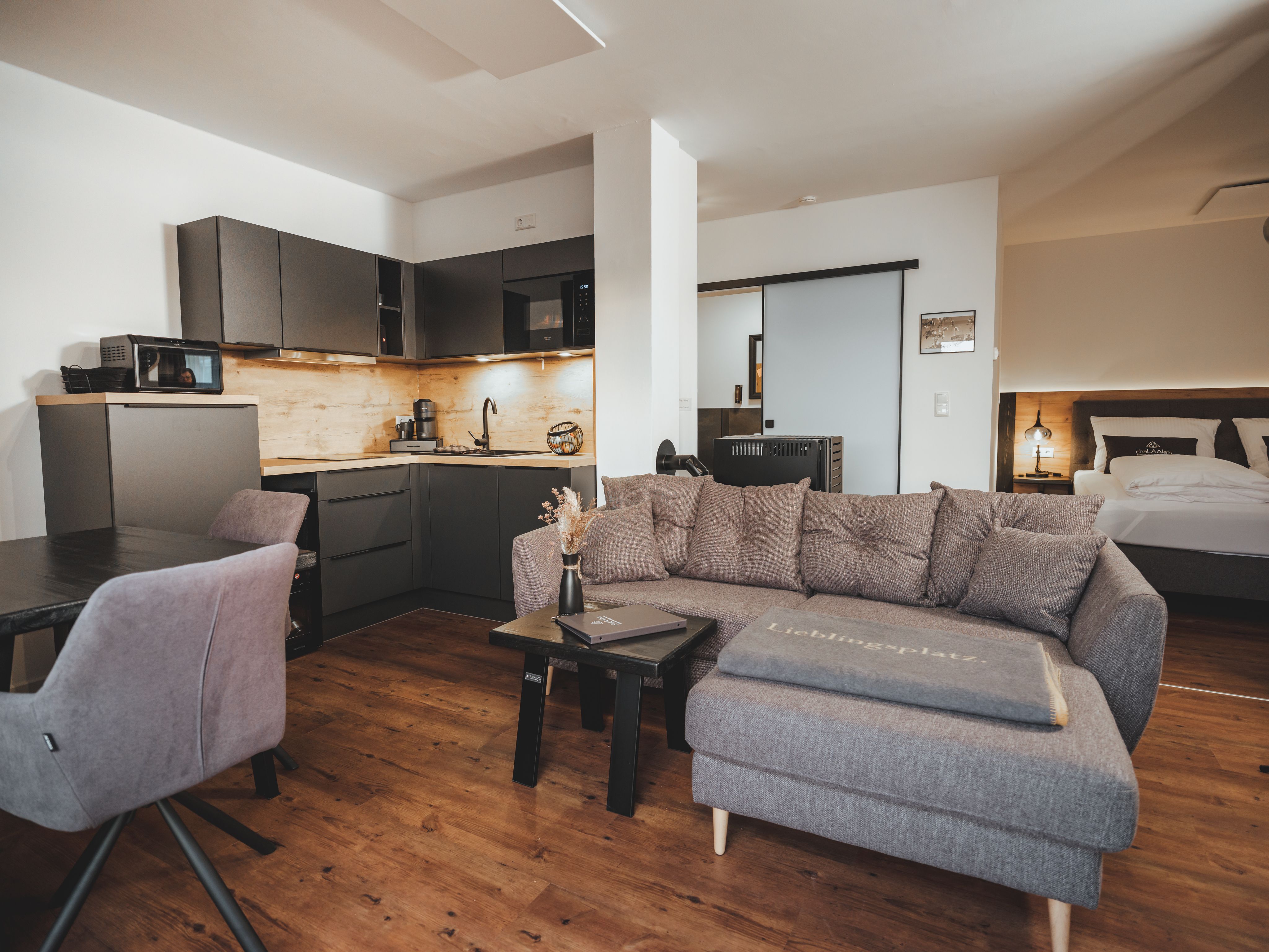 Modern living area with gray sofa, kitchenette and dining table.