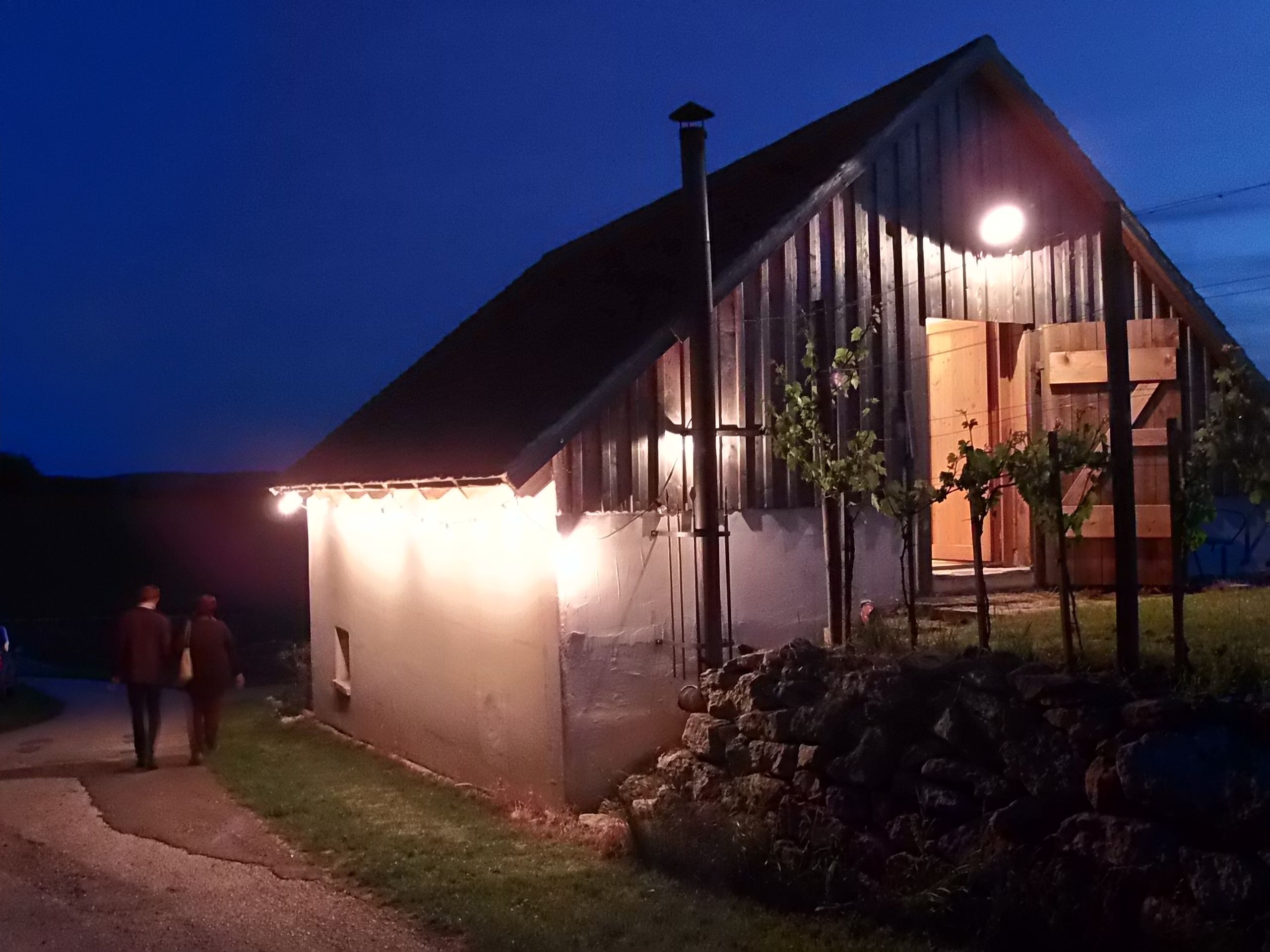 Illuminated wine cellar building at night with two people on a path.
