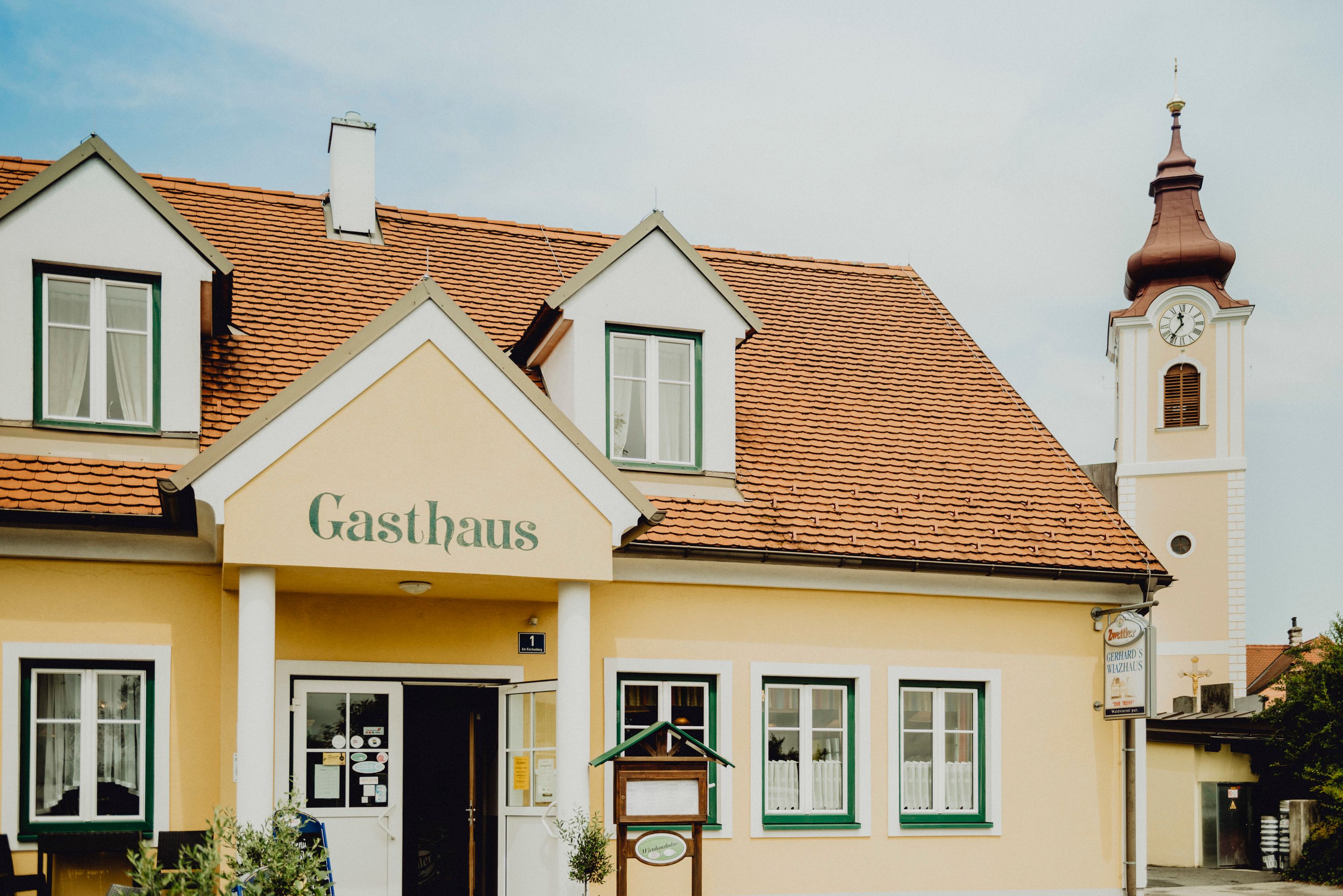 A yellow inn with red roof tiles and a church tower in the background.