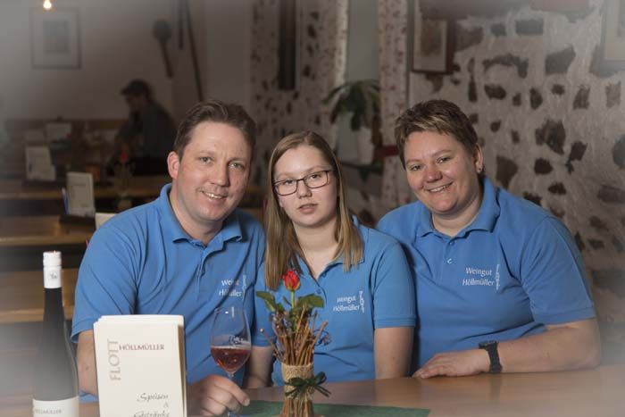 Three people in blue shirts sit at a table in a rustic room.