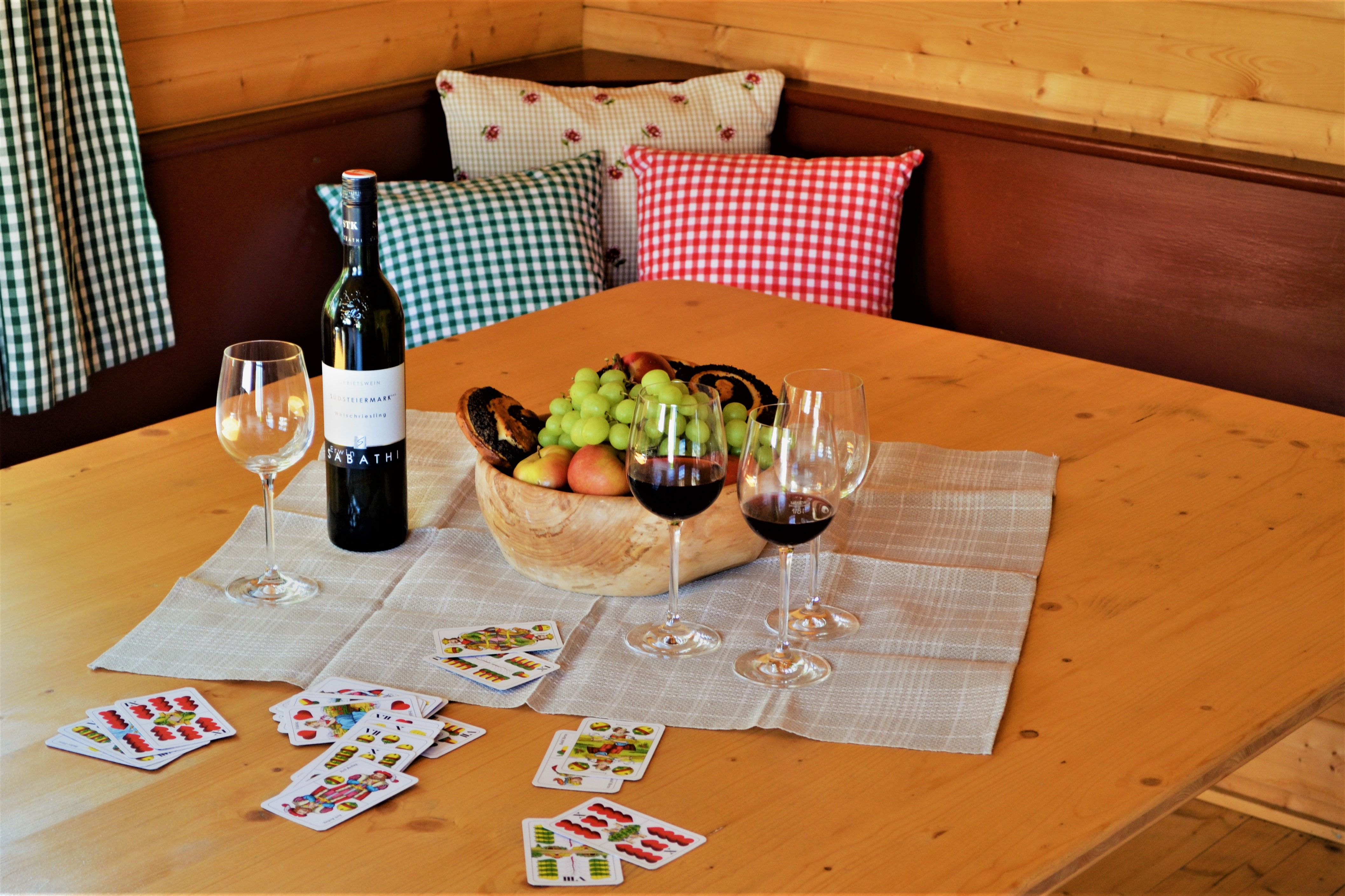 A table with wine bottle, wine glasses, fruit bowl and playing cards.
