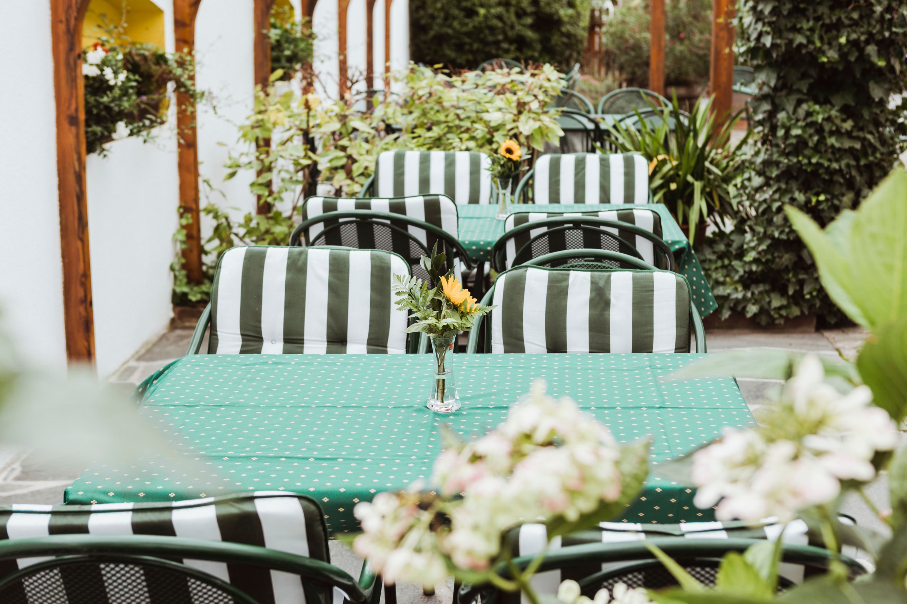 A cozy outdoor area with green and white striped chairs and green tablecloths, decorated with flower vases.