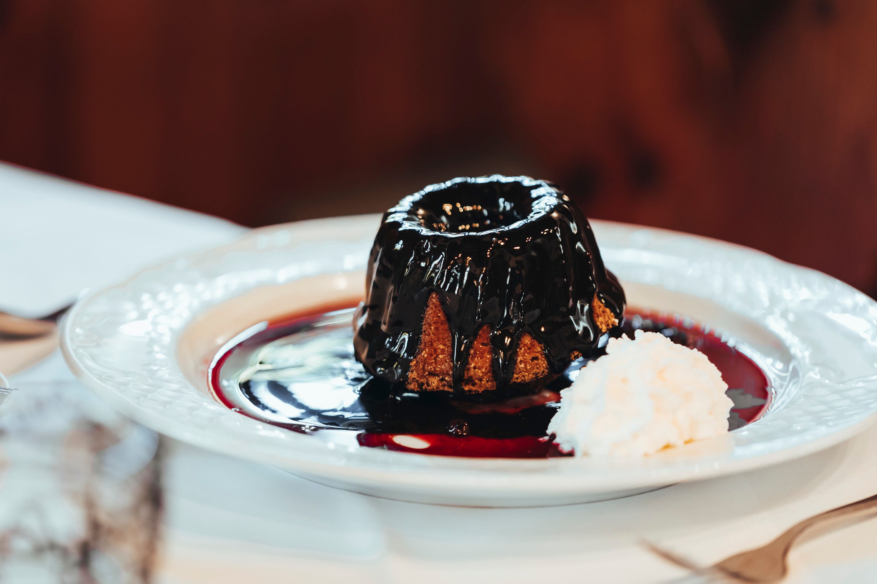 A Gugelhupf with chocolate sauce and whipped cream on a plate.
