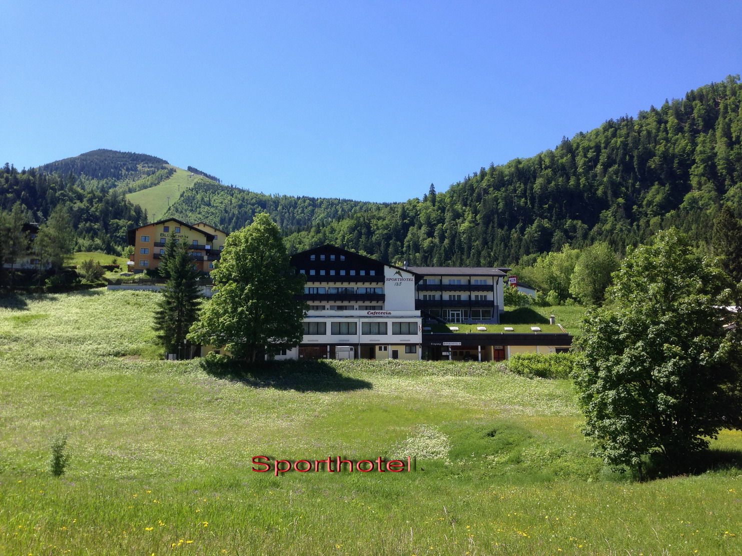 A sports hotel in a green mountain landscape with a blue sky.