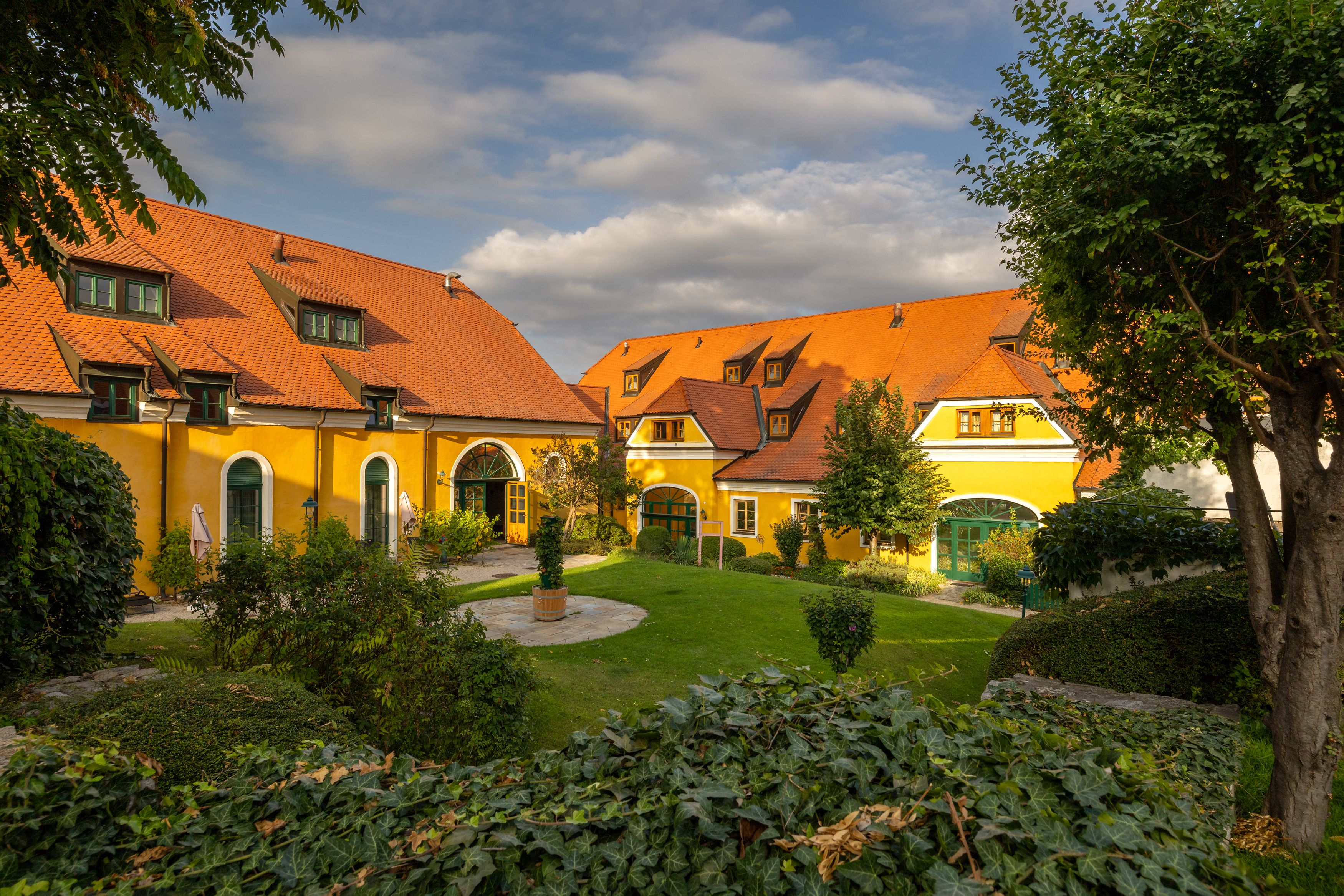 Yellow country estate with red roofs and well-tended garden.