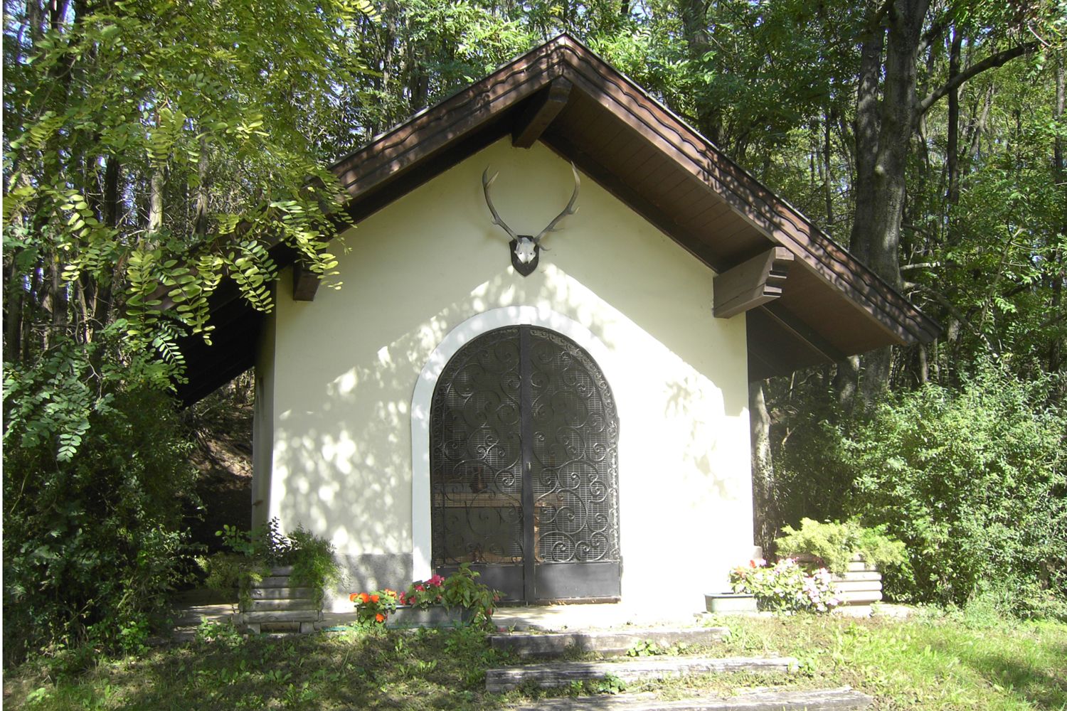 A small chapel in the forest with deer antlers above the door.