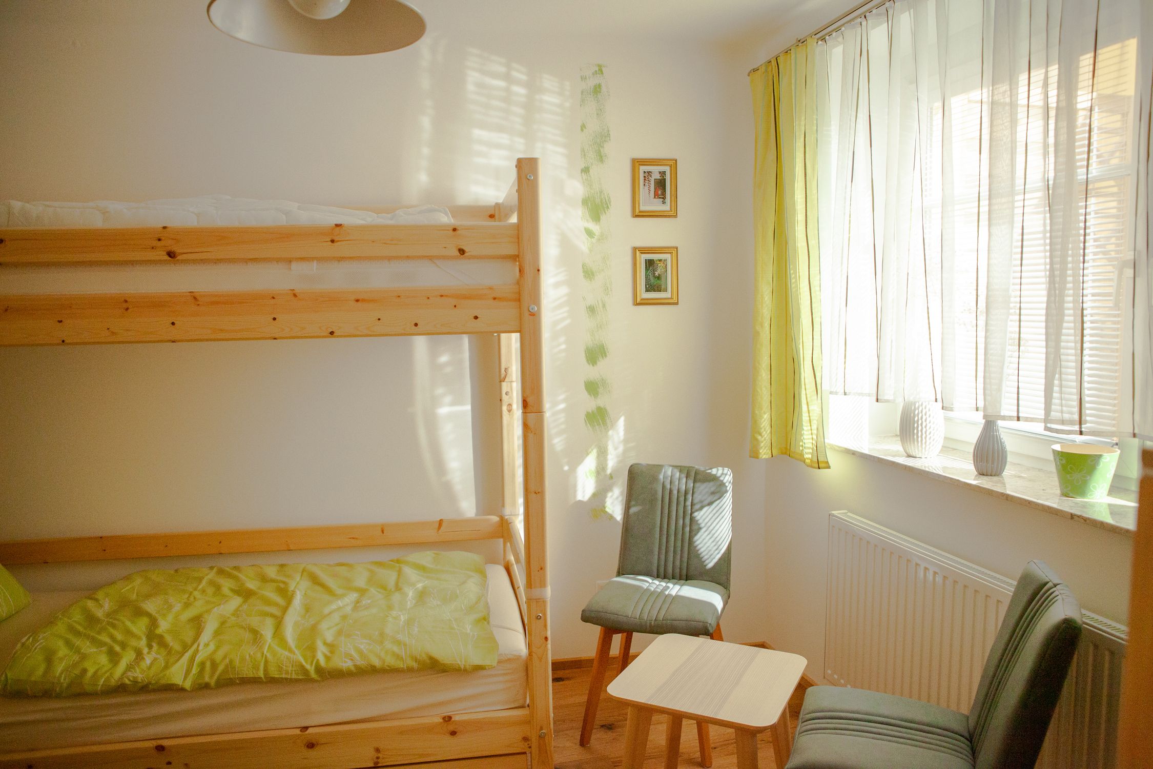 A bright room with a bunk bed, two chairs, a small table and a window with curtains.