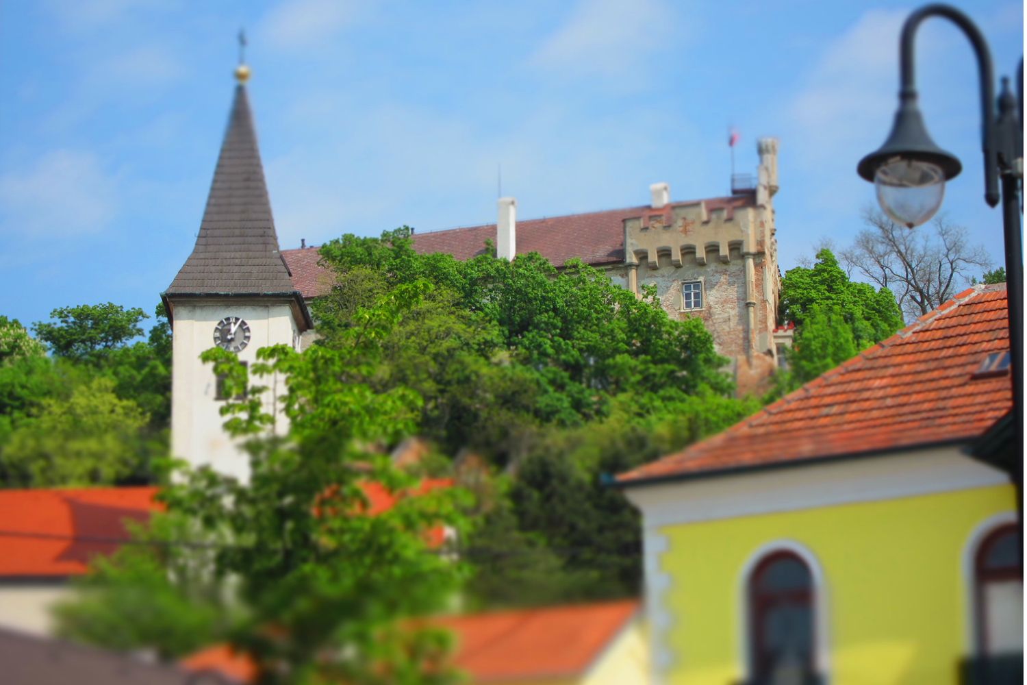 Church tower and castle behind trees, blue sky.