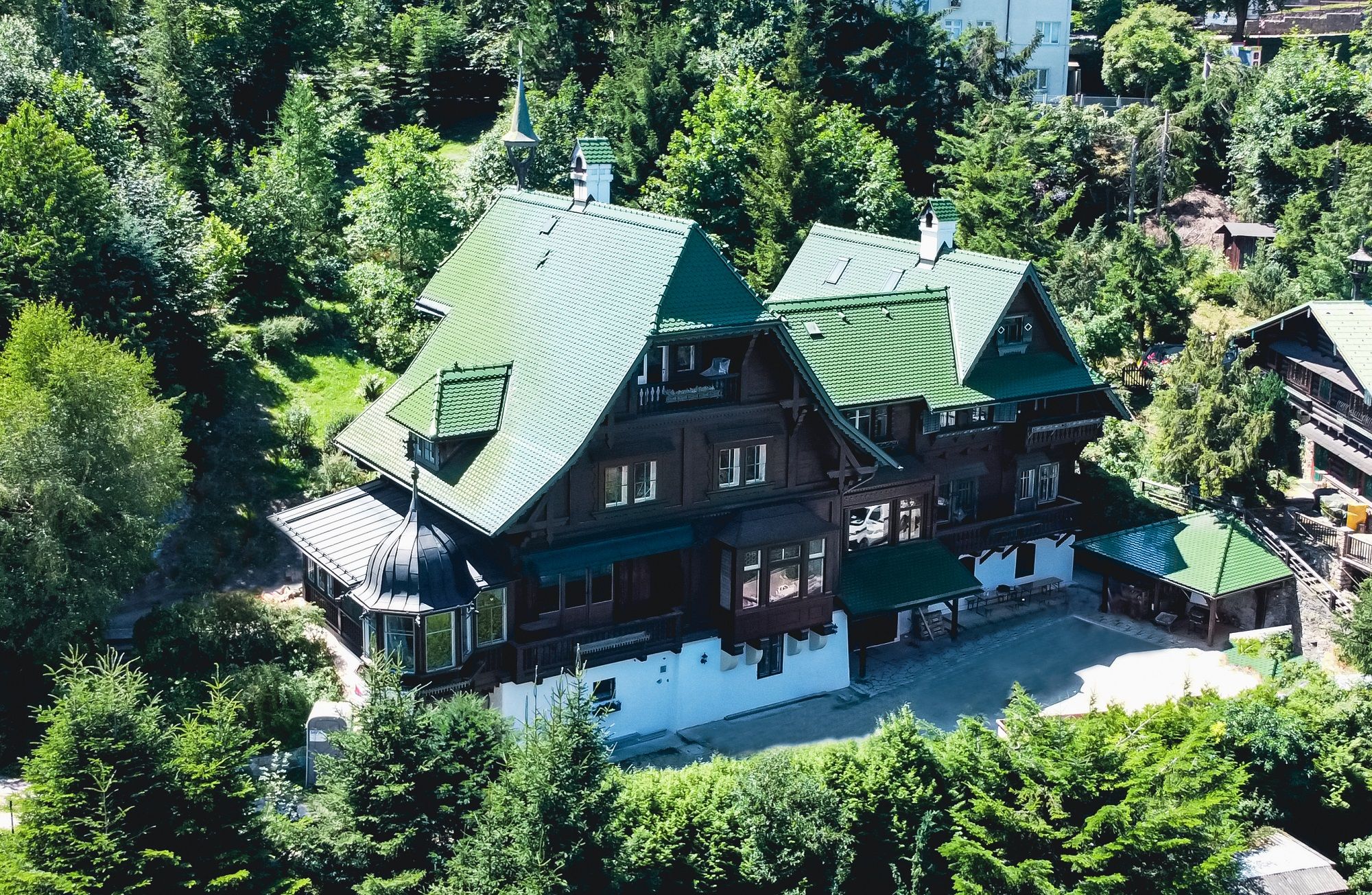 Aerial view of a large villa with a green roof, surrounded by trees.