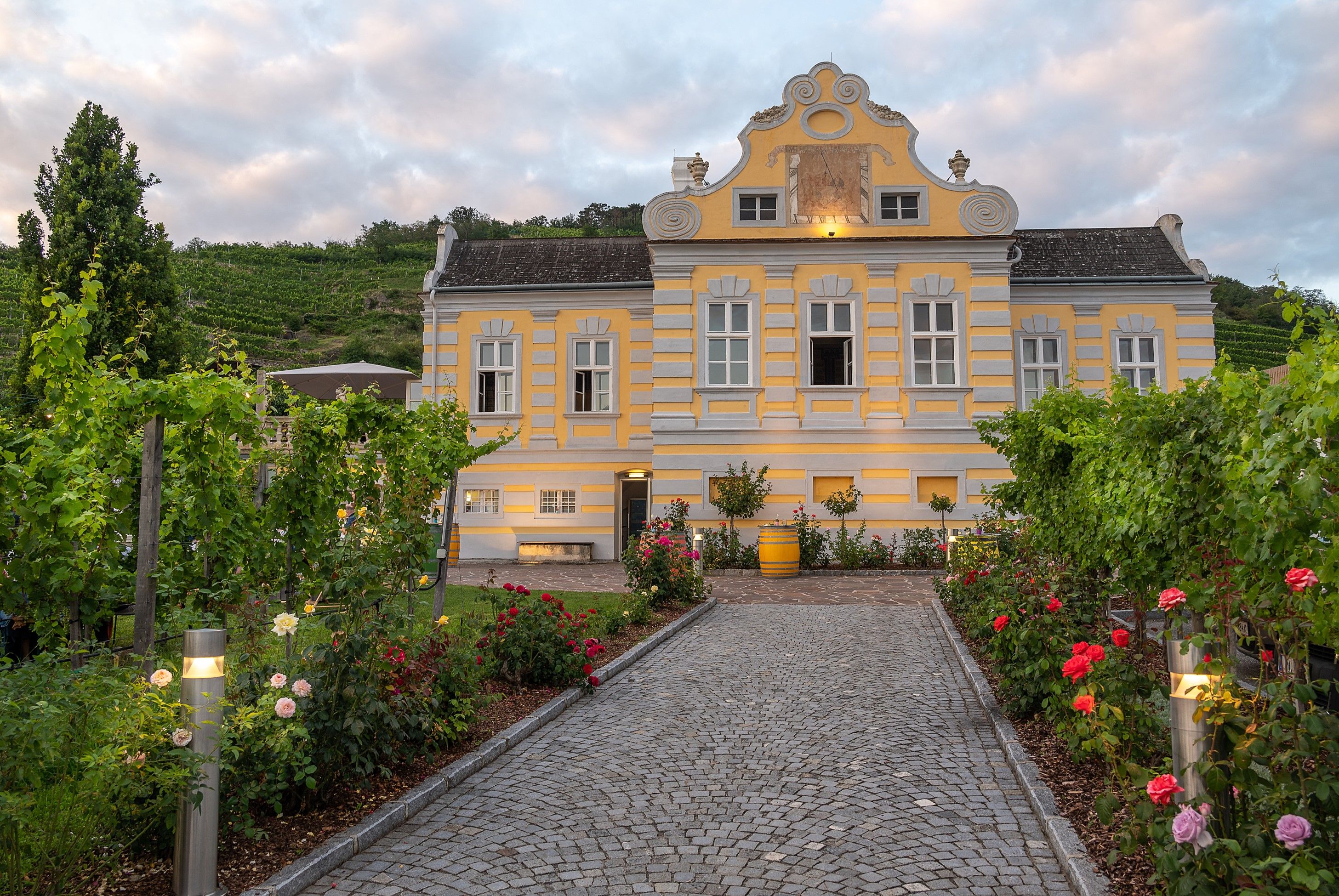 Yellow baroque building with garden and vines, twilight.
