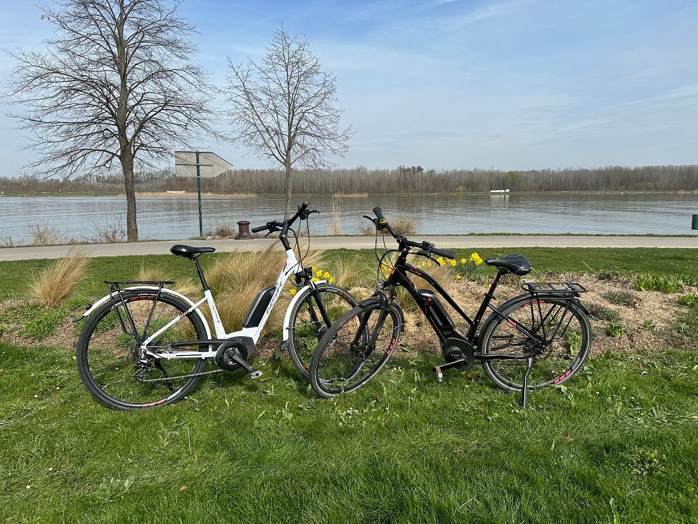 Two e-bikes are parked on a meadow in front of a river.