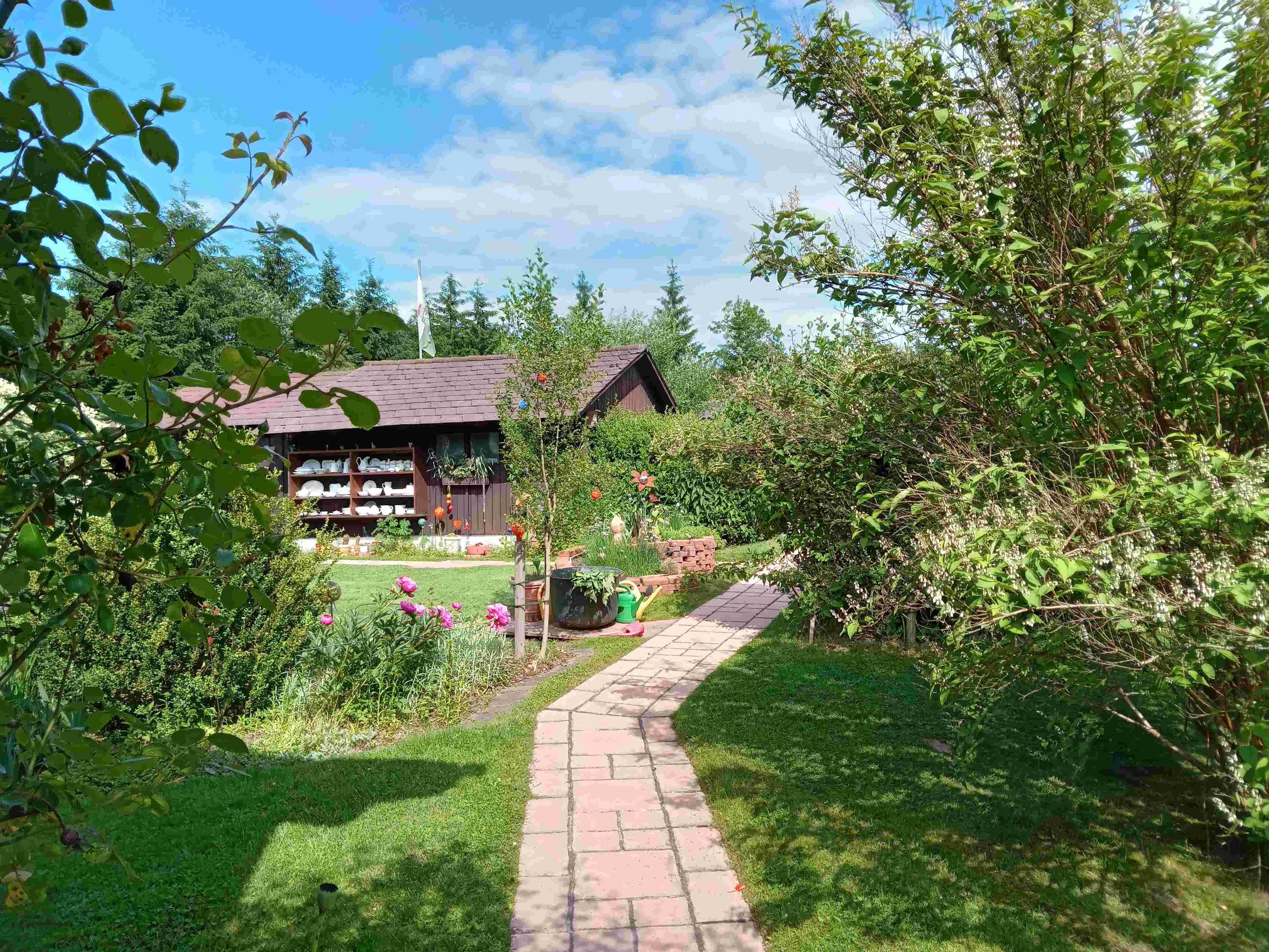 Garden with path, flowers and wooden hut in the background.