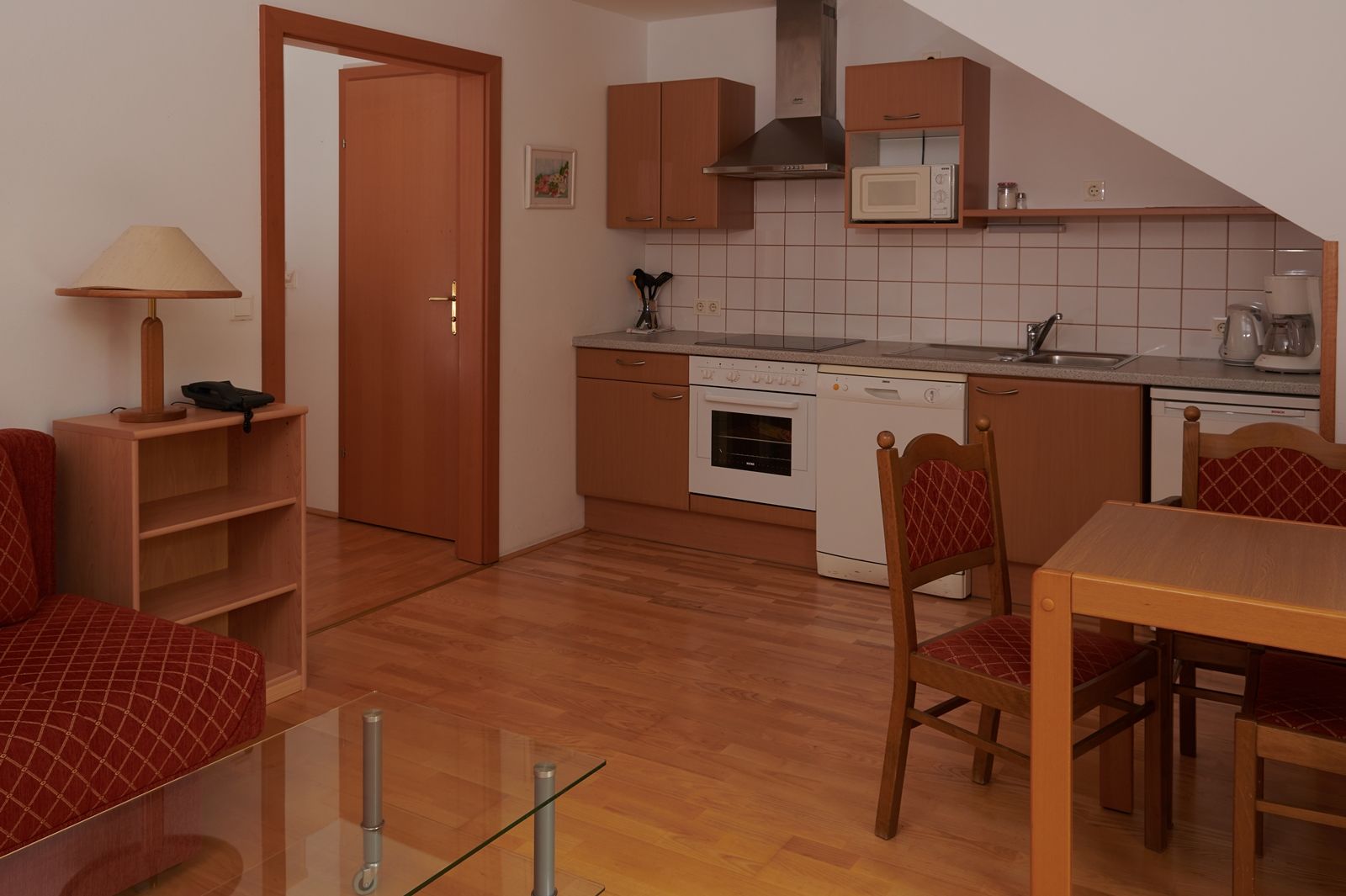 Compact kitchen with wooden cupboards, dining table and chairs, stove, sink and microwave.