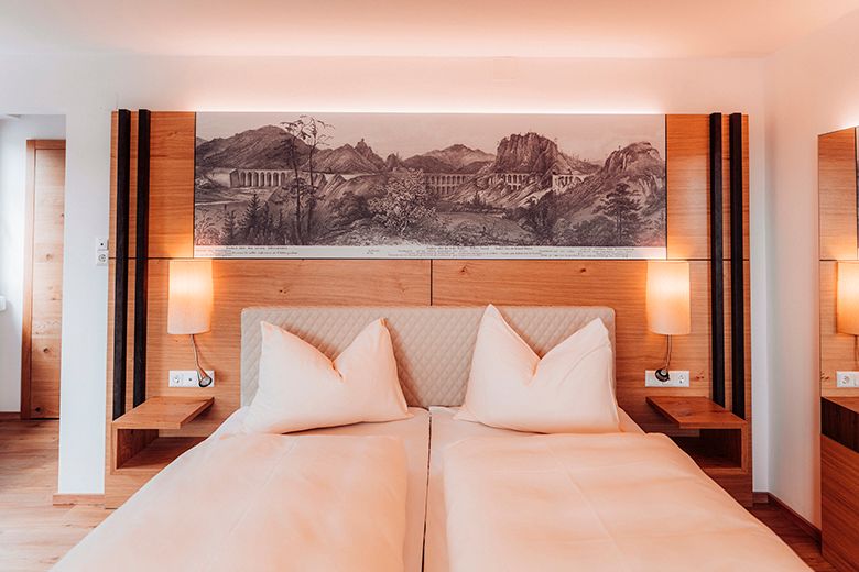 A modern double room with two beds, wooden furniture and a landscape painting above the bed.