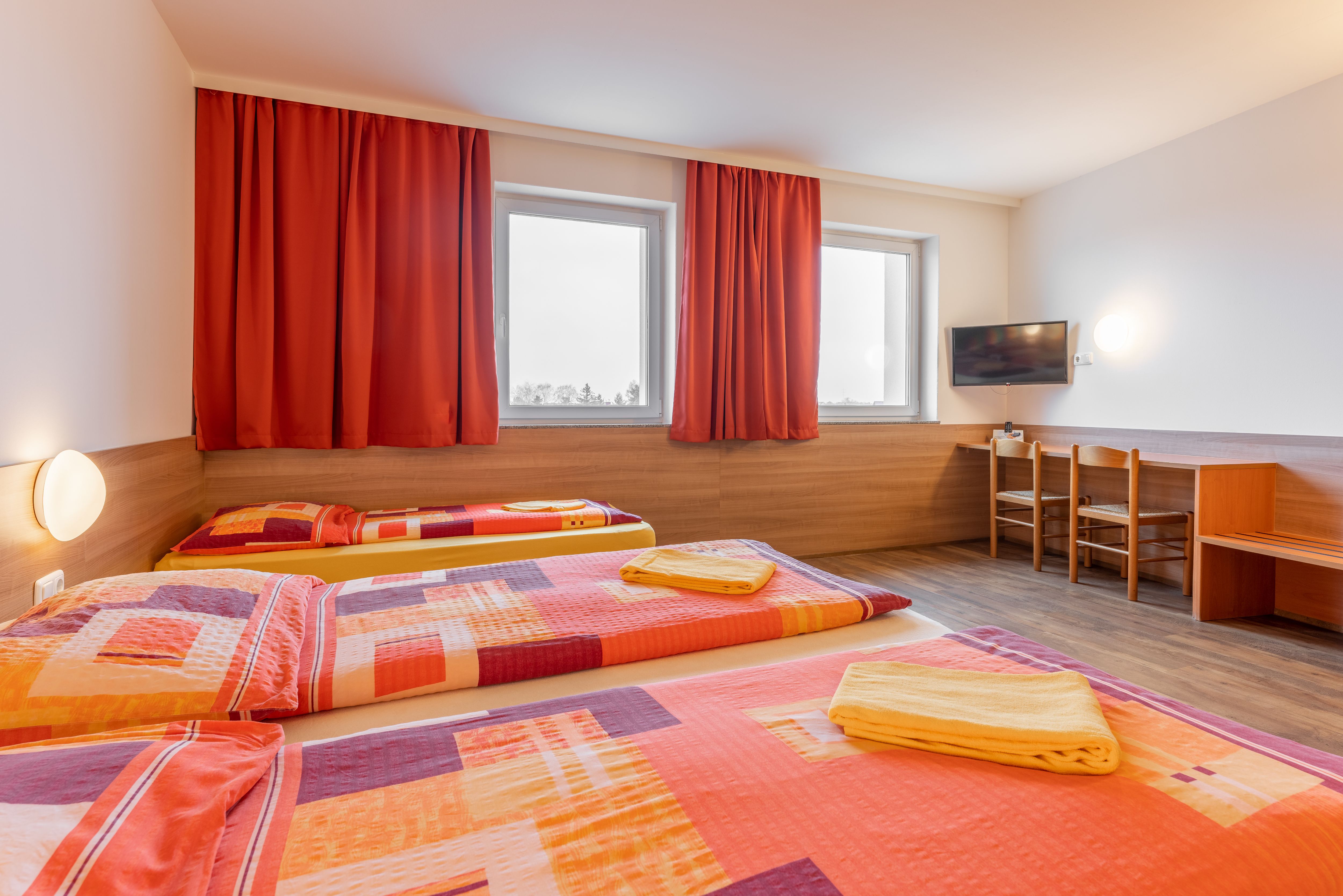 Hotel room with three beds, red curtains and a TV on the wall.